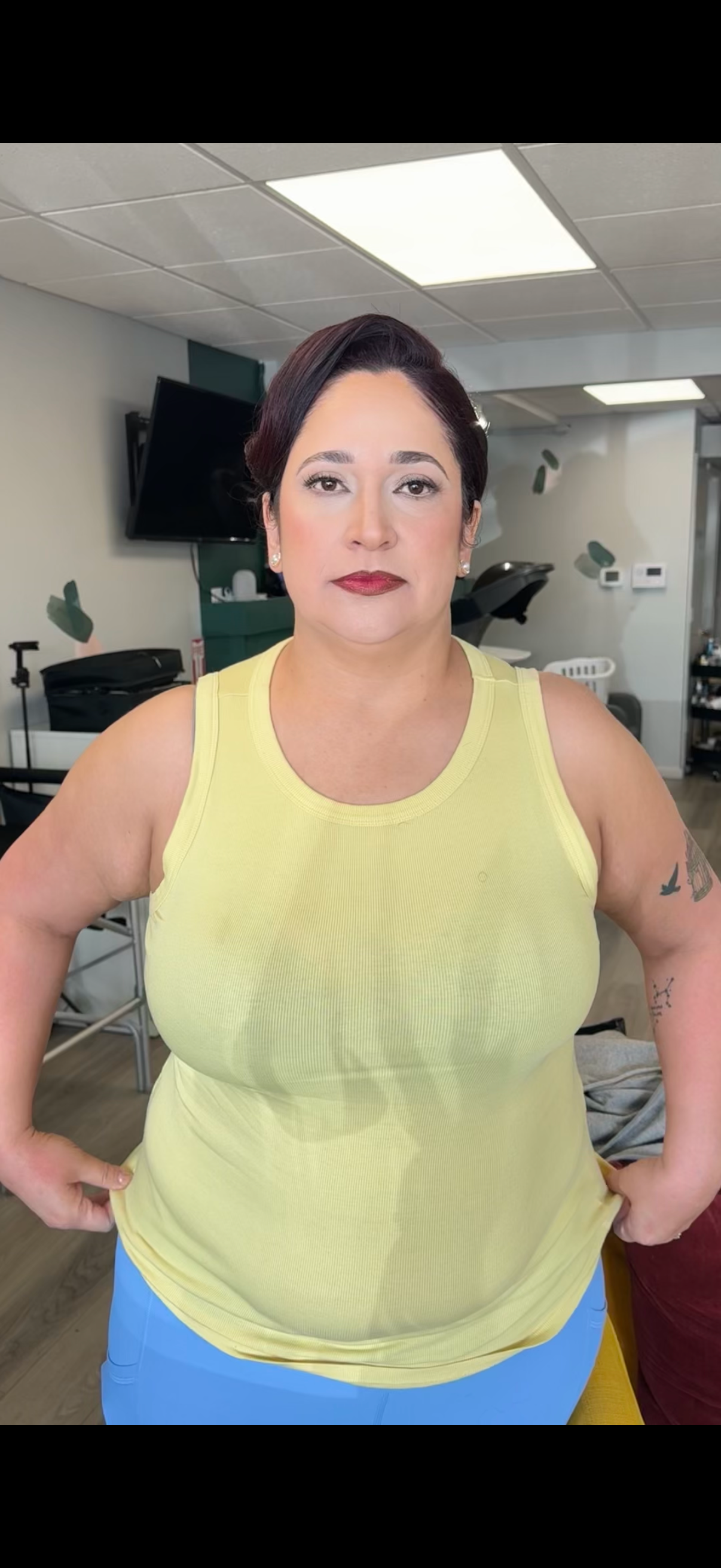 Posing in a bright yellow sleeveless top and blue bottoms in an indoor setting.