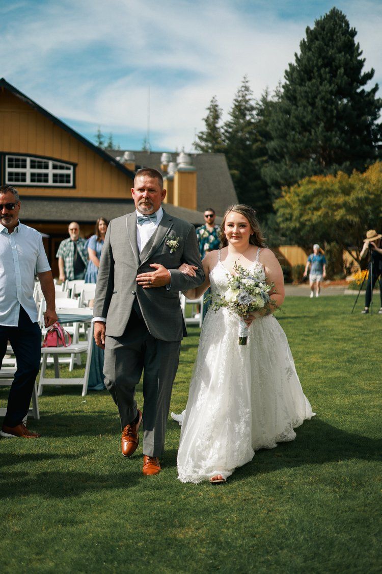 Wedding ceremony procession on a sunny lawn with attendants in blue dresses.