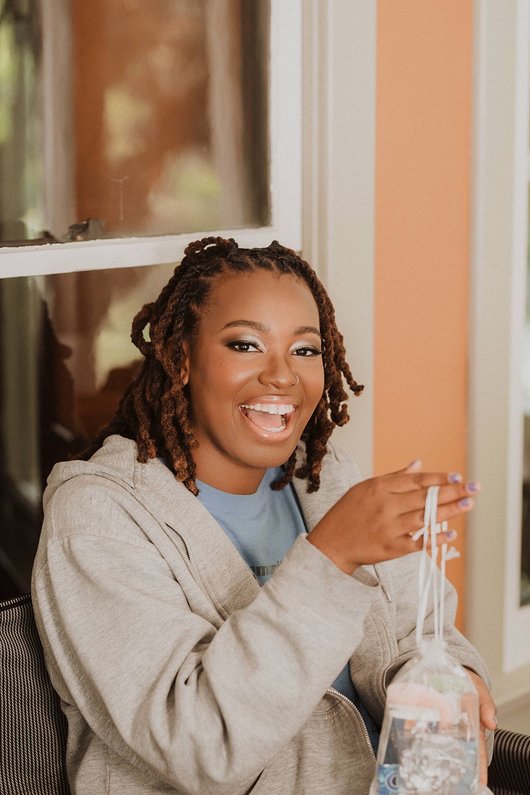 Person in a cozy gray sweater laughs while drinking from a glass with a straw.