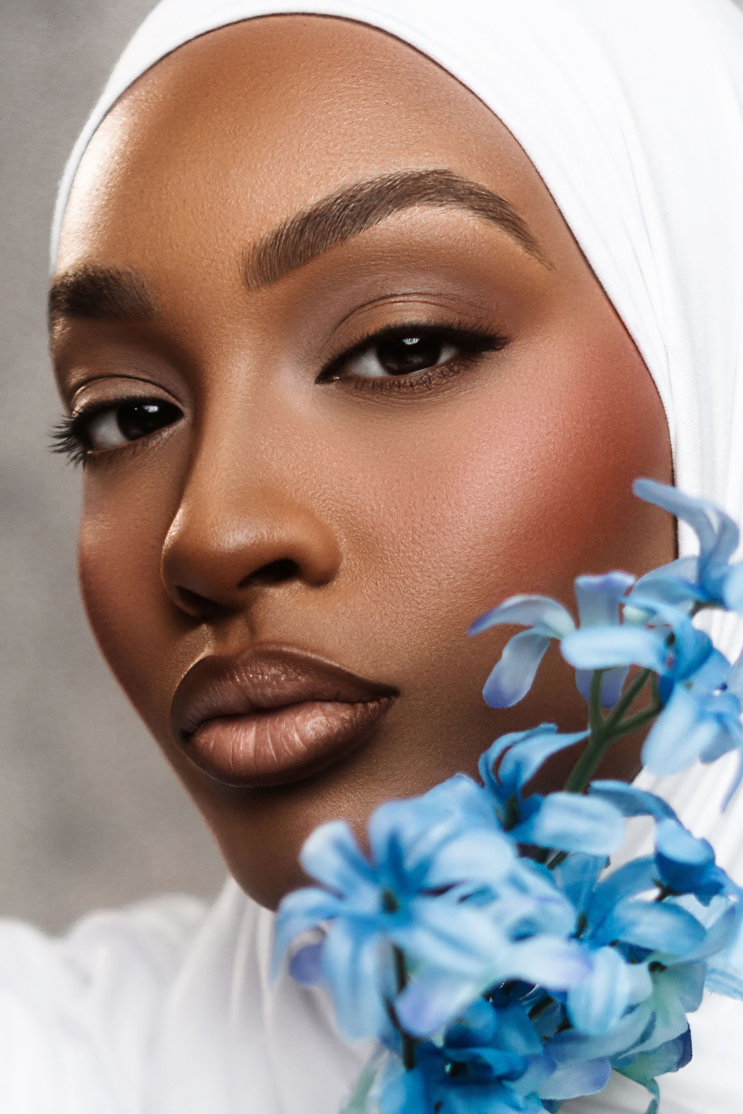Beautiful portrait with soft makeup look featuring vibrant blue flowers against a light background.