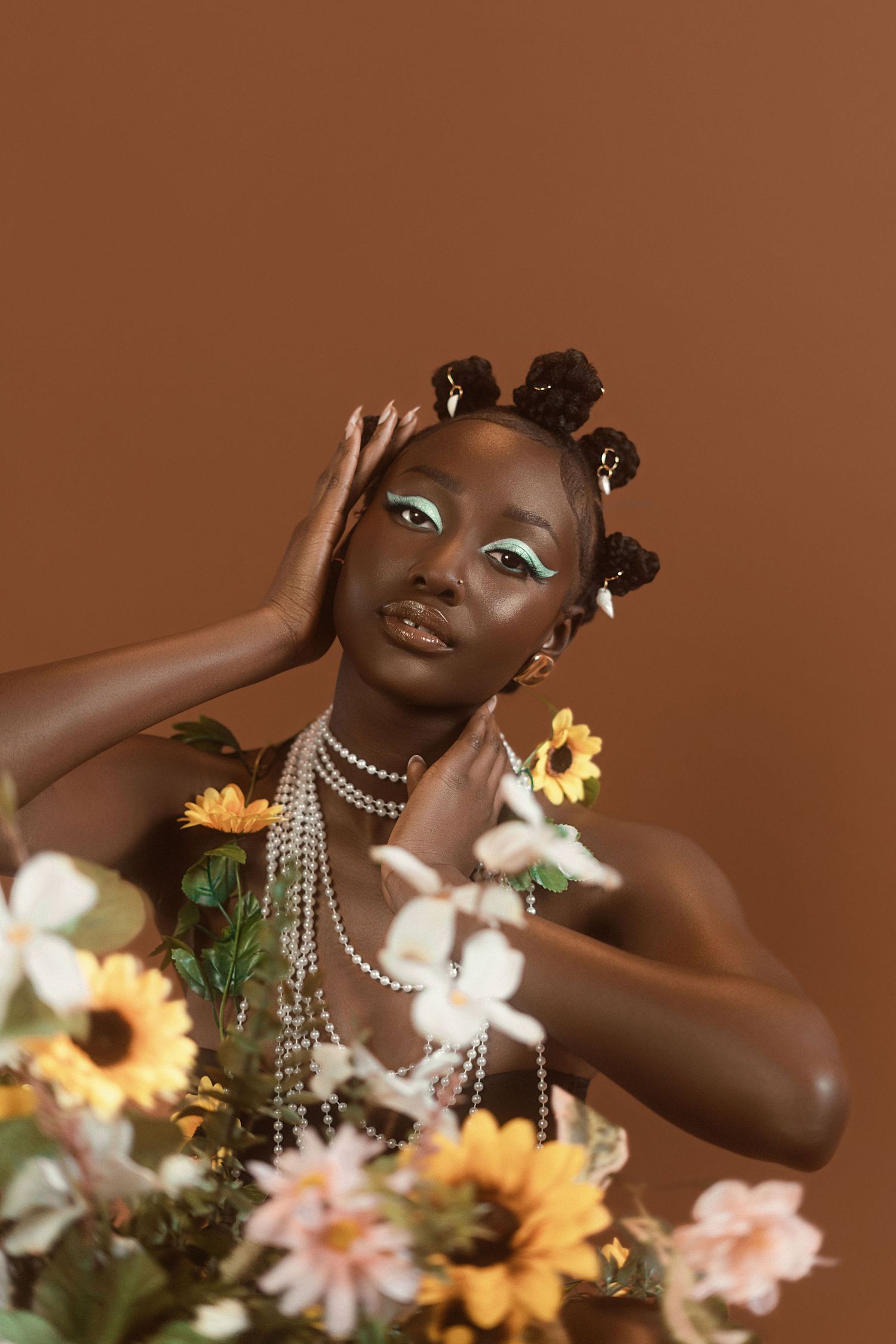 Artistic portrait with sunflowers and pearls against brown background featuring elegant styling and natural hair.