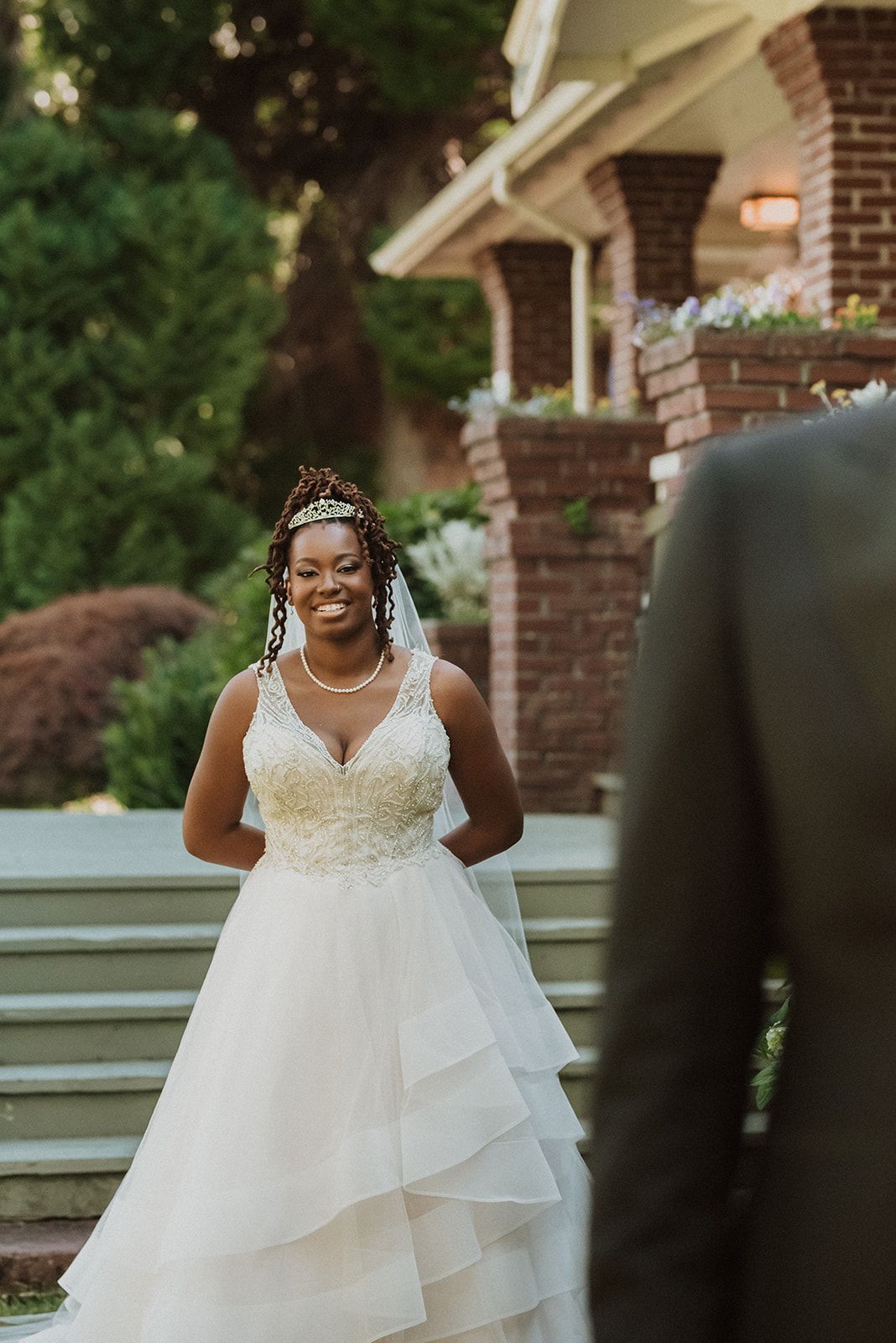 Bride in an elegant lace wedding dress smiles during outdoor ceremony.