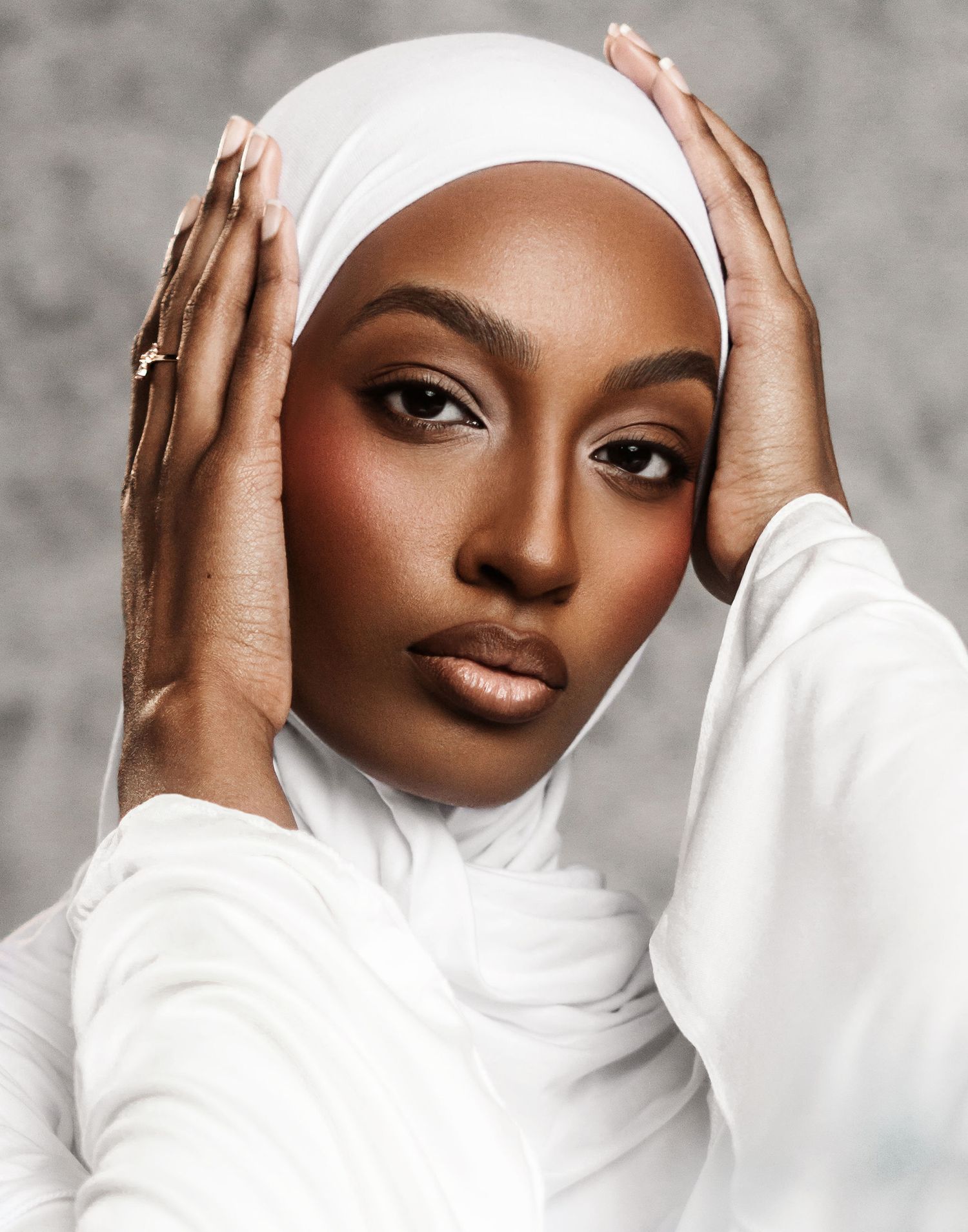 Elegant portrait with white headscarf and dramatic makeup against grey background.