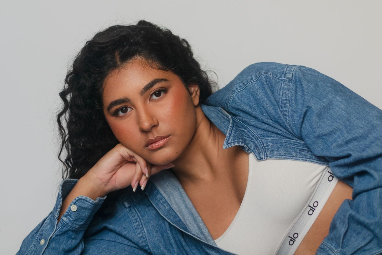 Fashion portrait in denim jacket against light grey studio background.