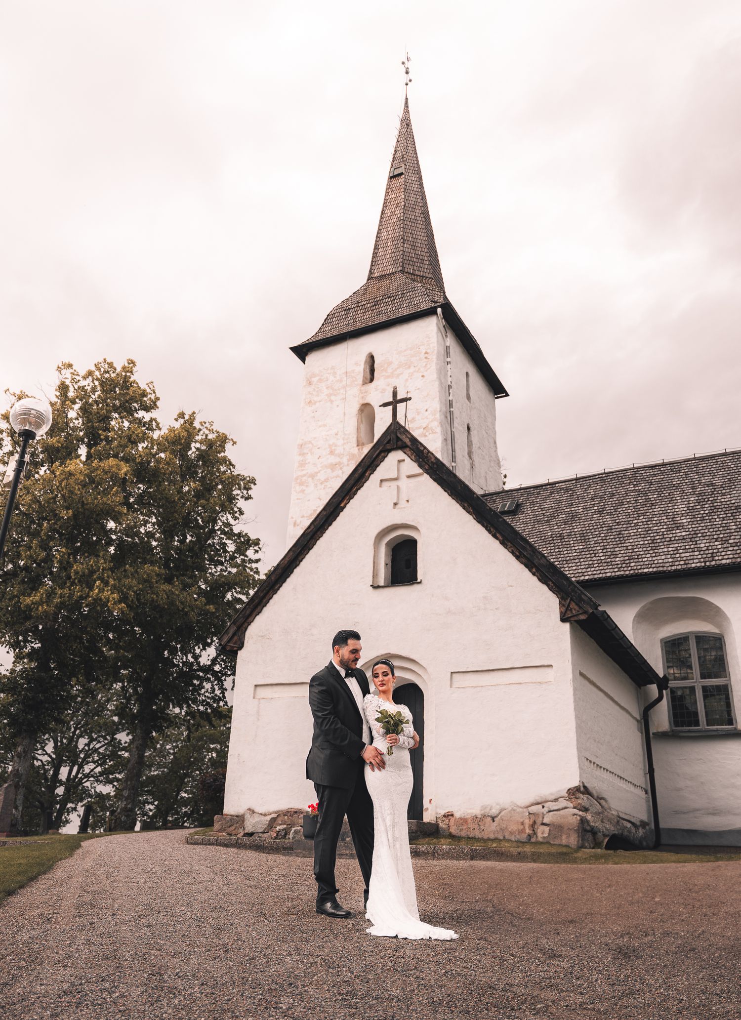 brudpar poserar med en vit kyrka i bakgrunden
