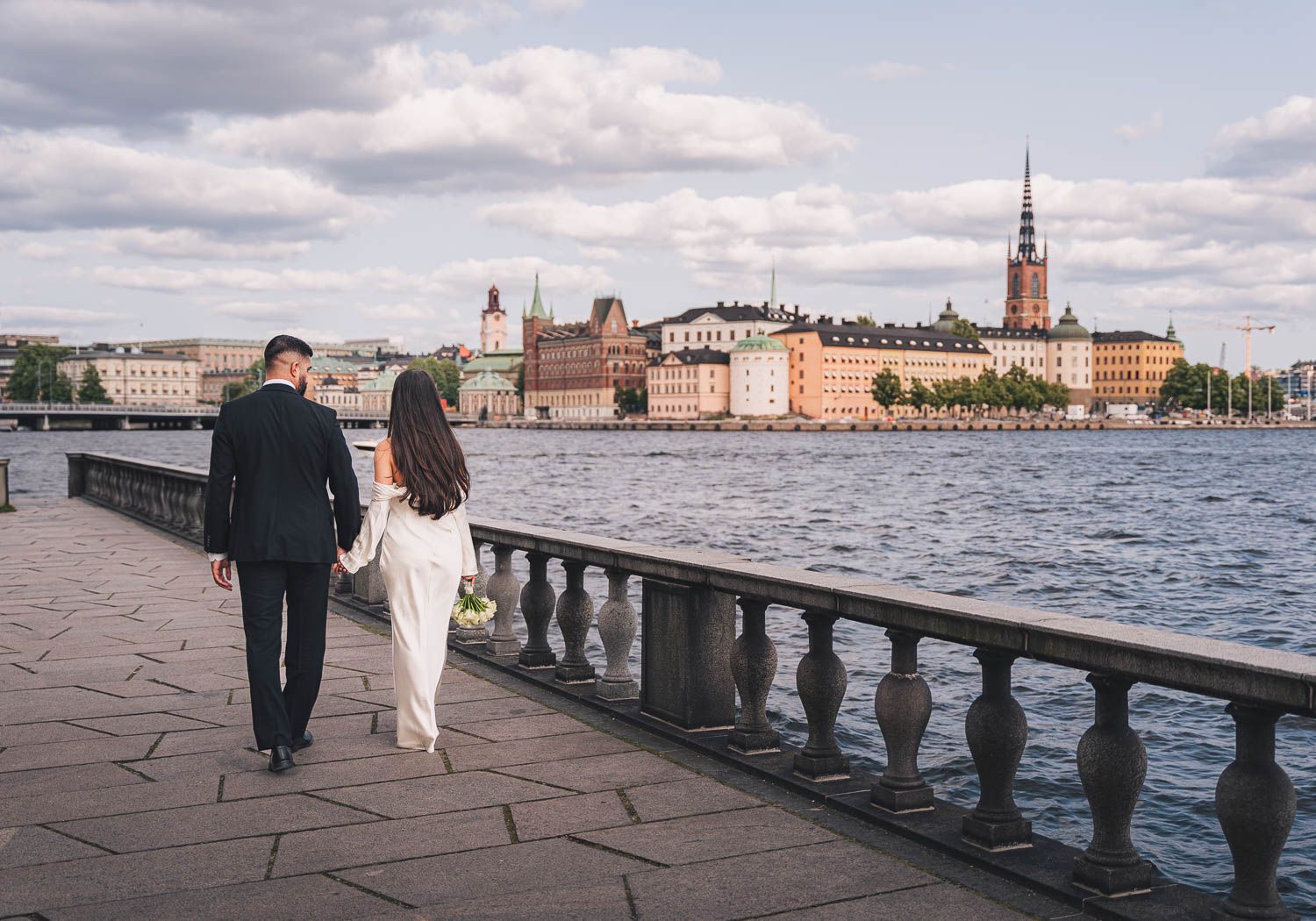 Brudpar går hand i hand utanför Stockholms stadshus och tittar ut mot Riddarfjärdens strand