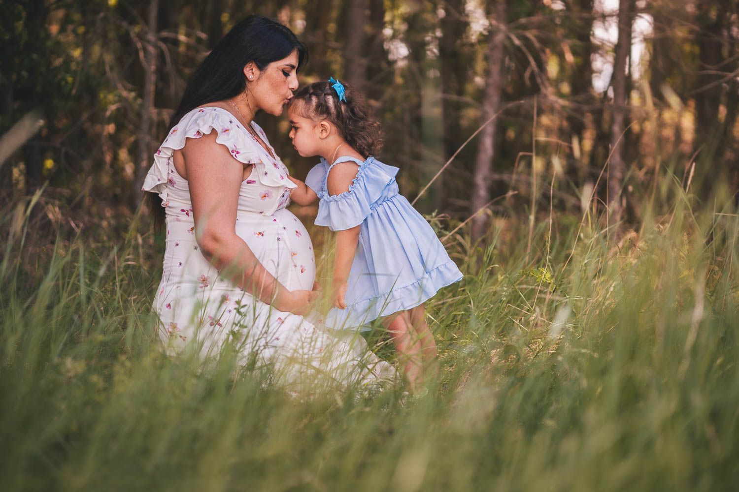 En gravid kvinna pussar hennes dotter på pannan under en somrig familjefotografering i Eskilstuna