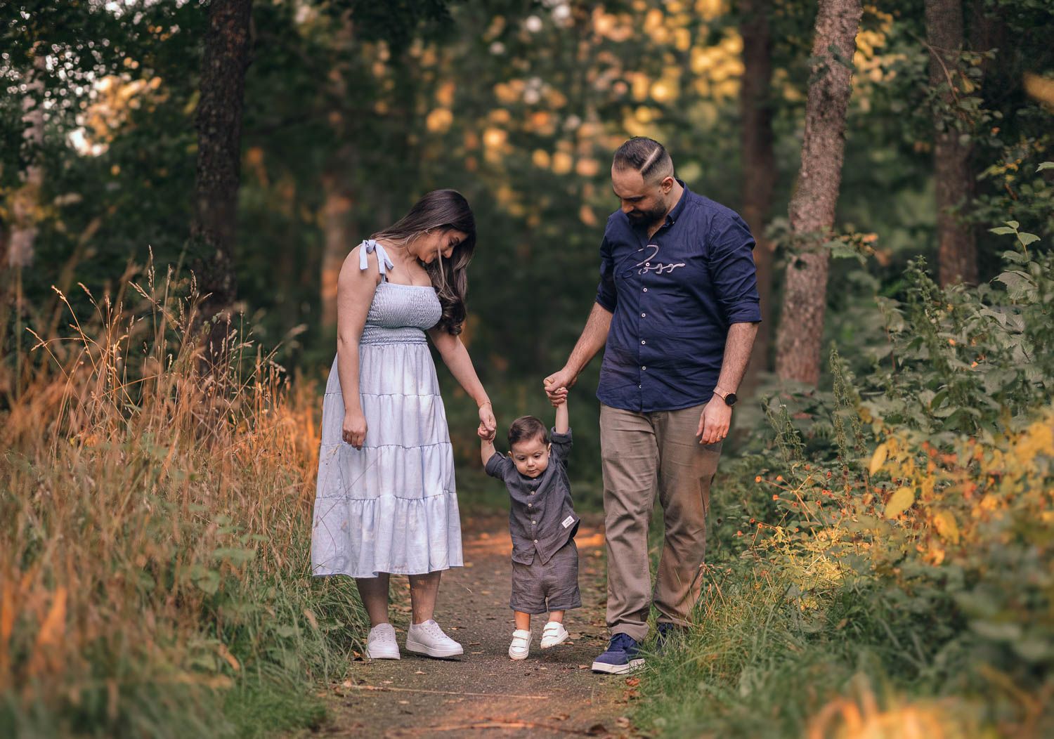 pappa och mamma går hand i hand med sin ett åriga son i skogen