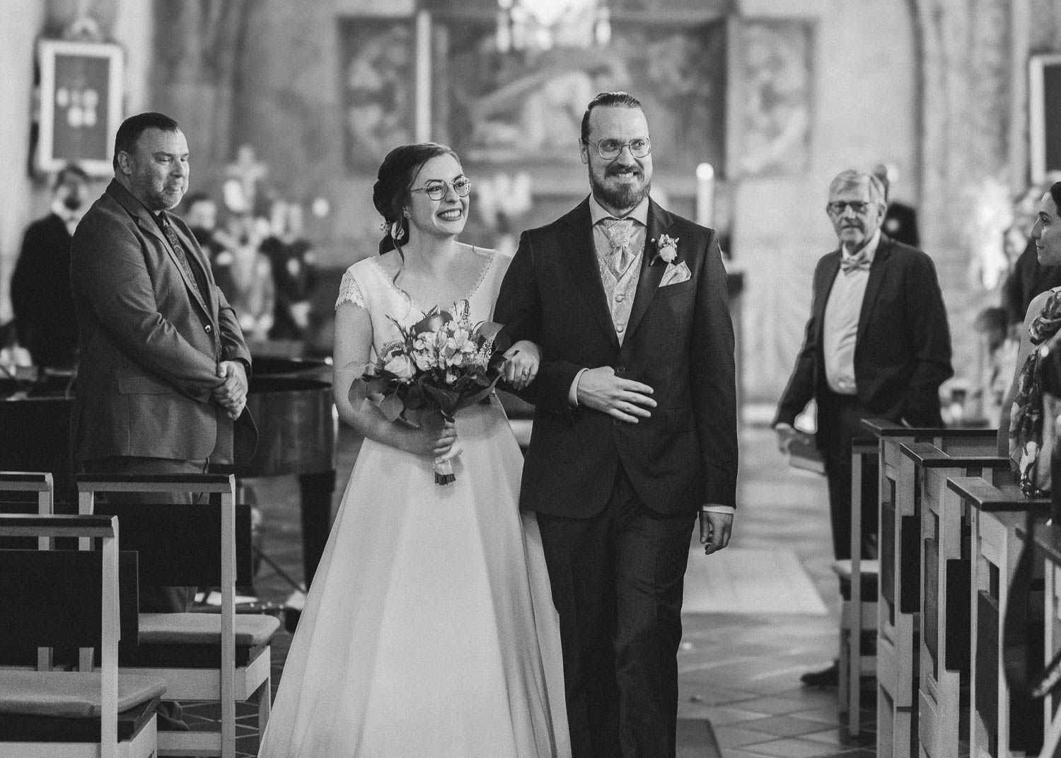 brudpar på väg ut från kyrkan och tittar glatt på gästerna efter en bröllopsceremoni