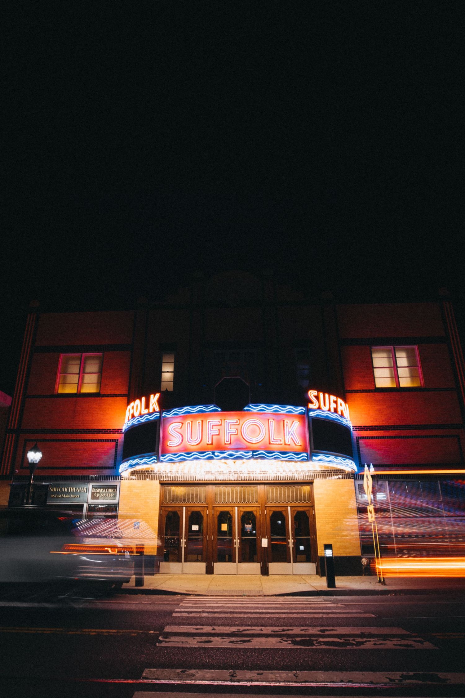 Suffolk Theater illuminated marquee sign glowing at night with colorful neon lights on dark street.