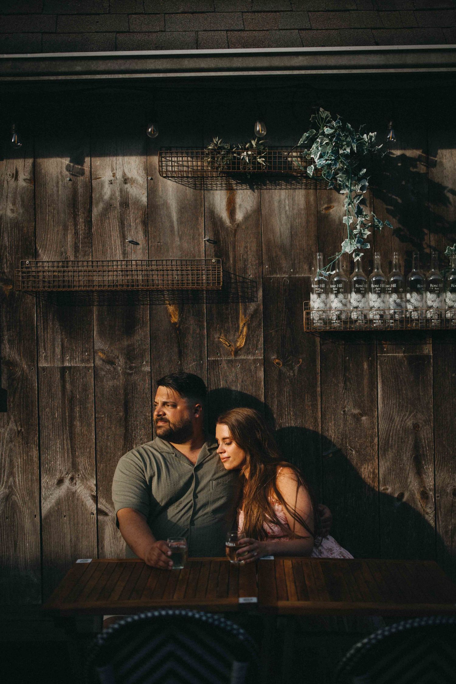 Couple sitting closely together at a wooden table in a warmly lit rustic bar setting.