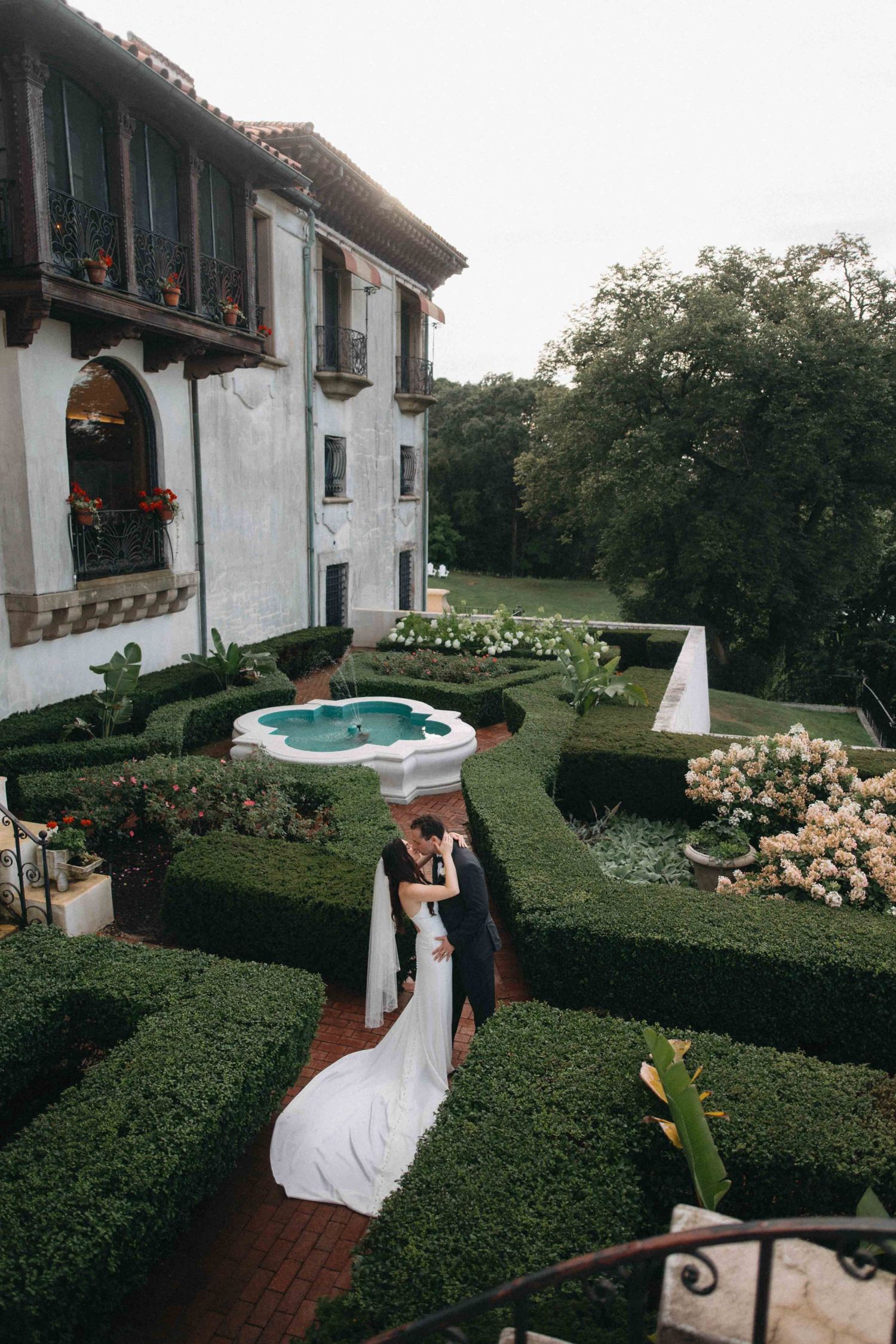 Bride and groom share romantic kiss in elegant Italian-style garden courtyard at sunset.