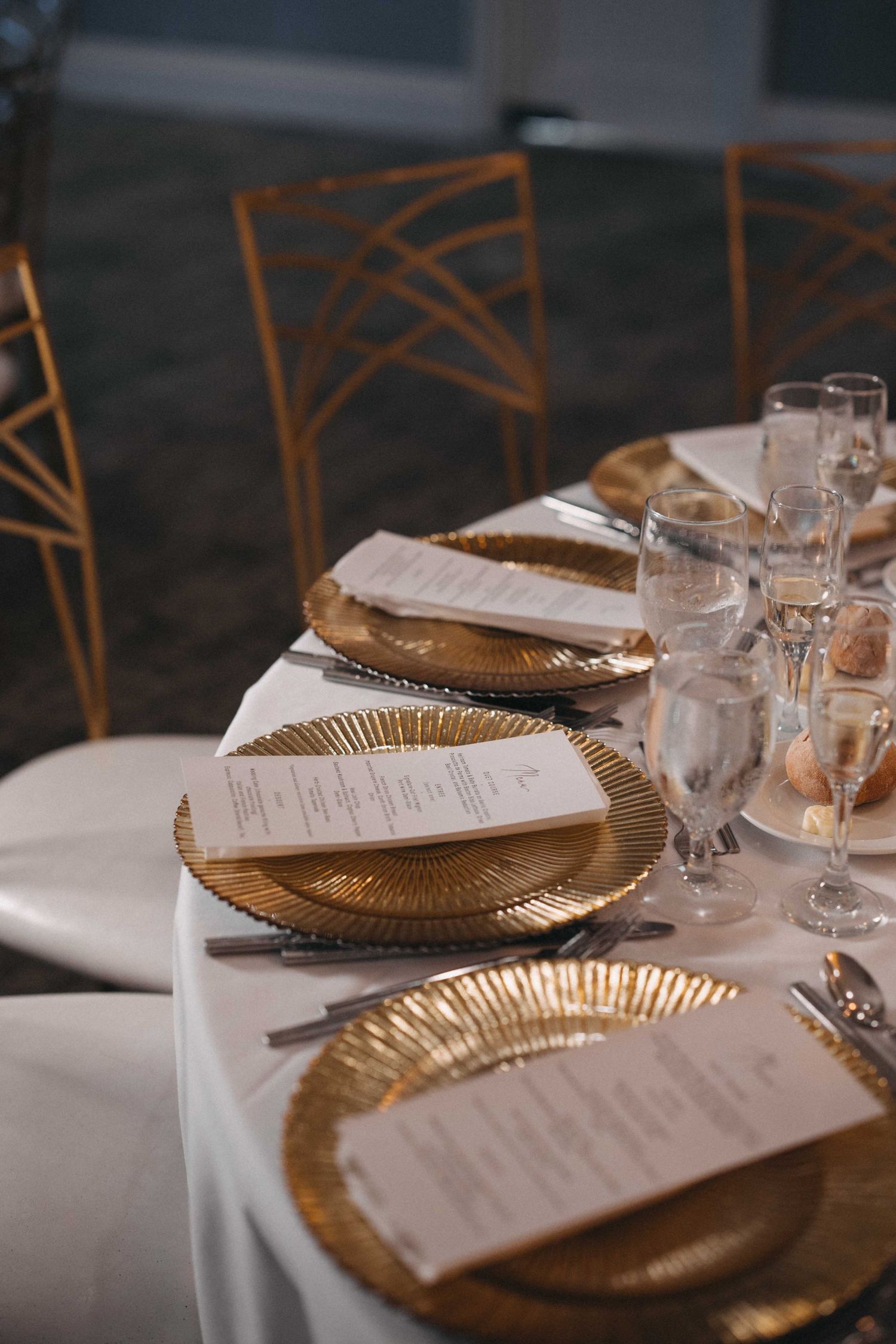 Elegant wedding reception table set with gold charger plates and white menu cards.