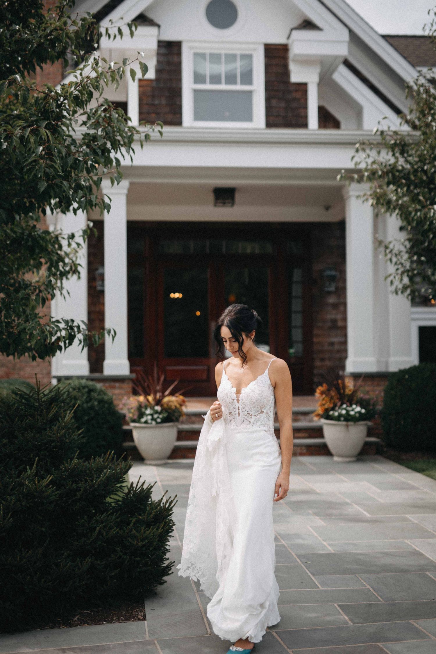 Bride in a backless lace wedding dress walking along a stone path in front of a craftsman home.