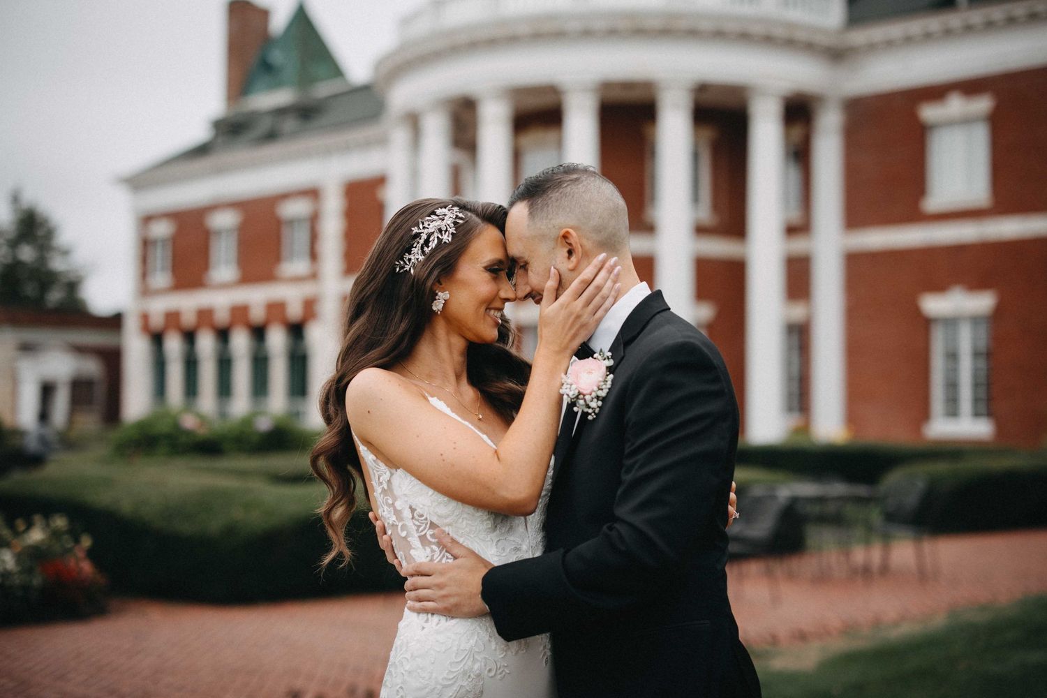 Bride and groom share tender moment outside elegant red brick colonial wedding venue.