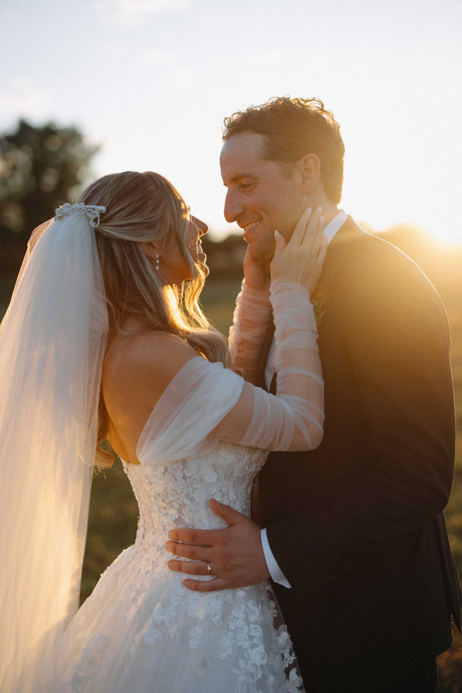 Smiling bride and groom sharing tender moment bathed in warm golden sunset light.