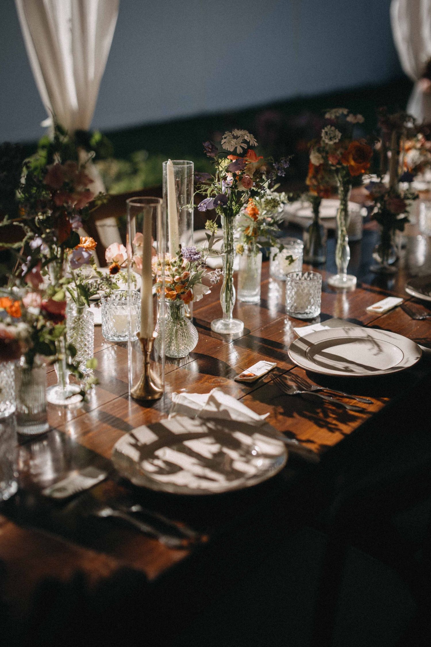 Elegant wedding table setting with crystal glassware, taper candles, and wildflower arrangements.