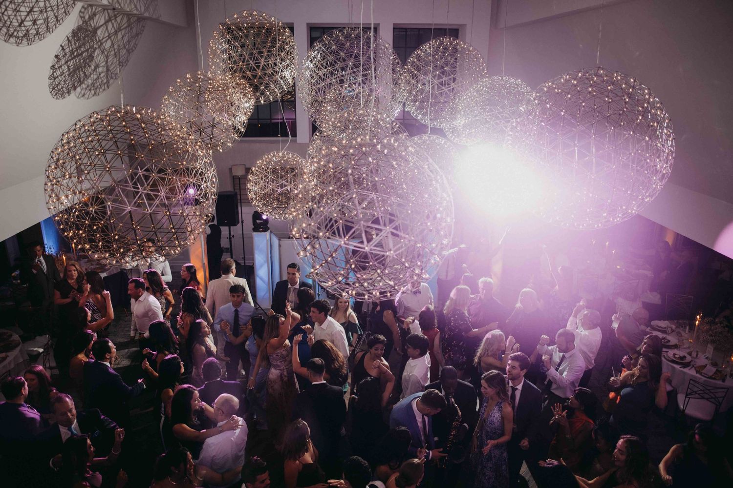 Aerial view of elegant wedding reception with sparkling spherical chandeliers and guests dancing below.