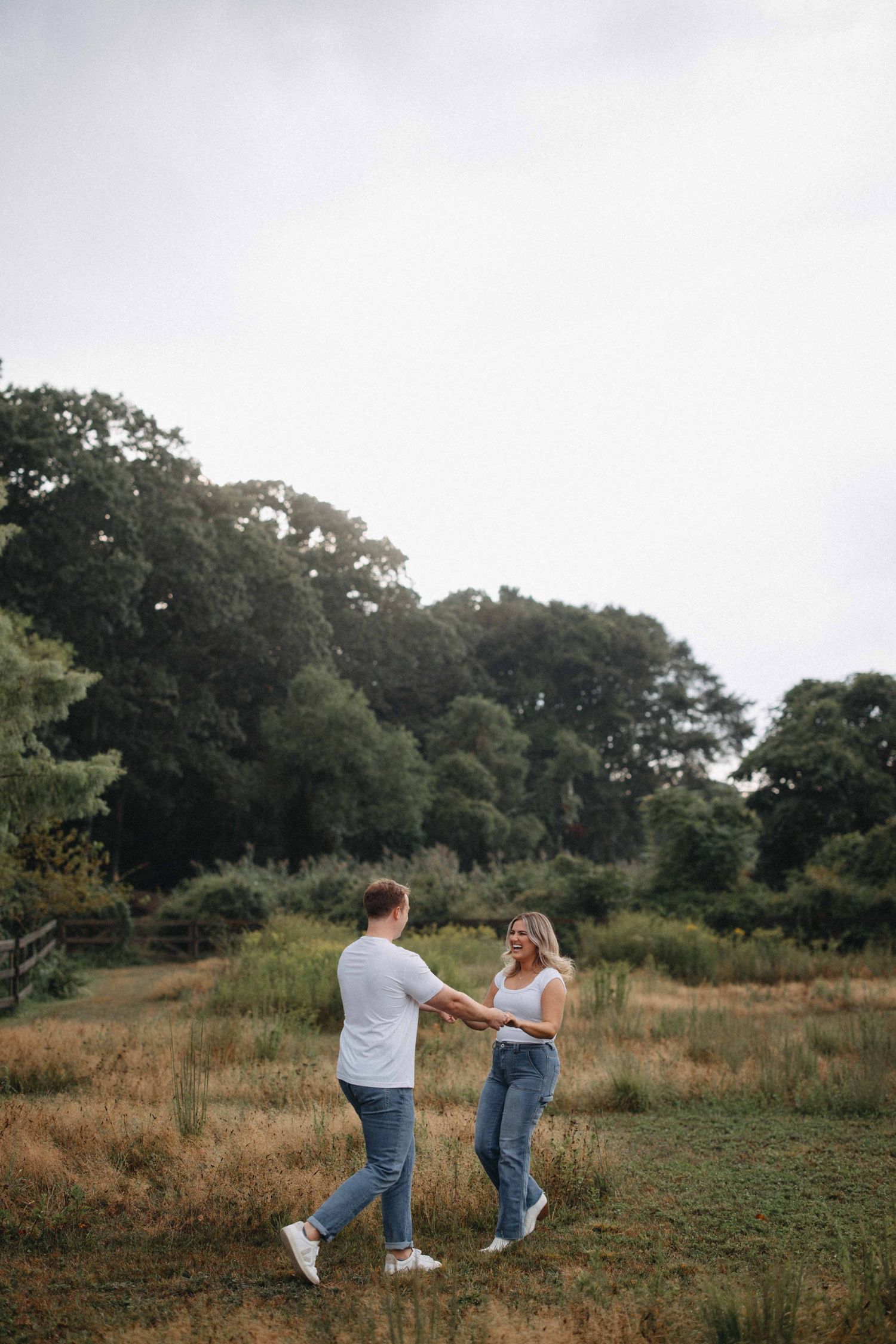Couple laughing and holding hands while dancing in a lush green meadow.