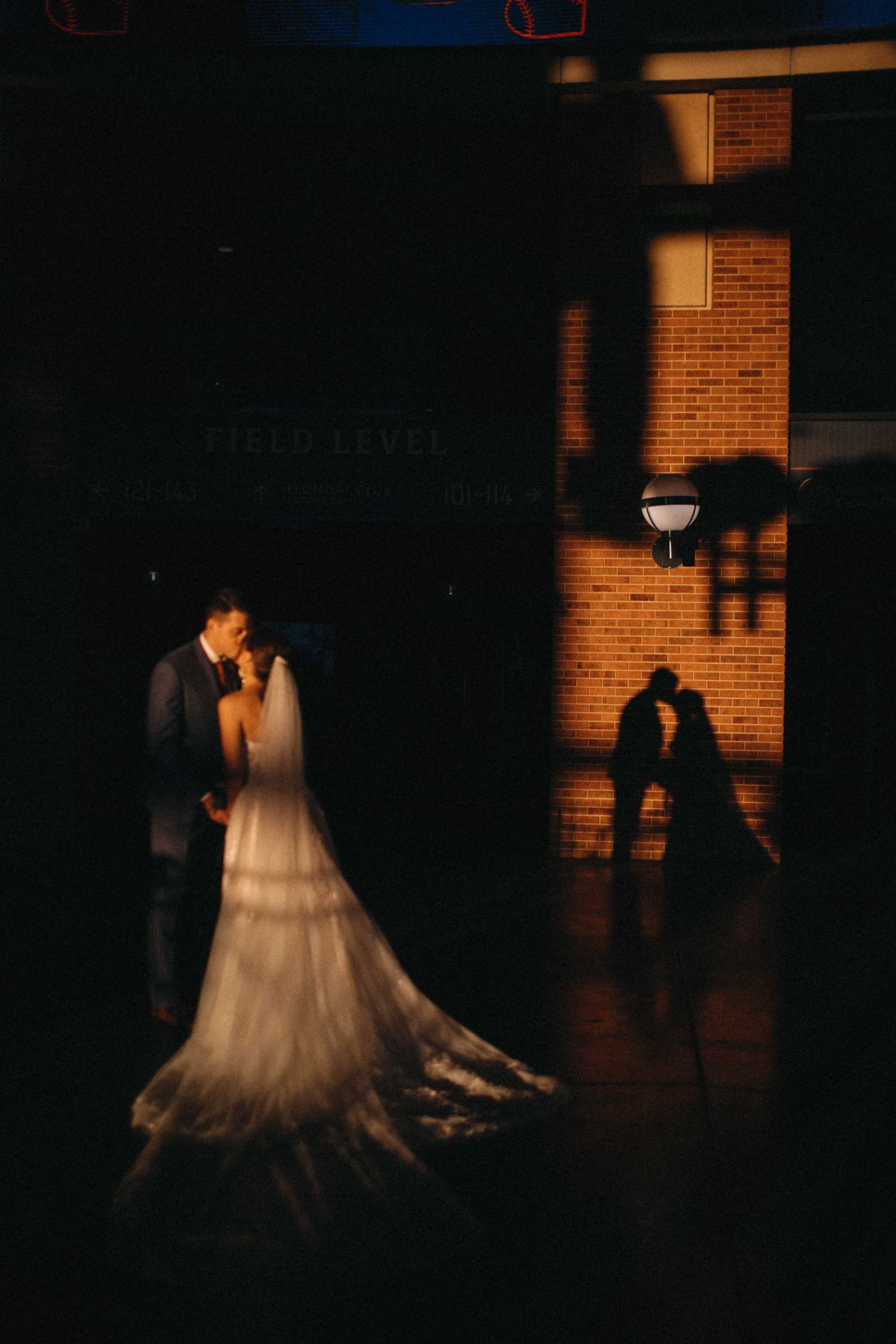 Bride and groom sharing a romantic kiss with their silhouette reflected on a brick wall at night.