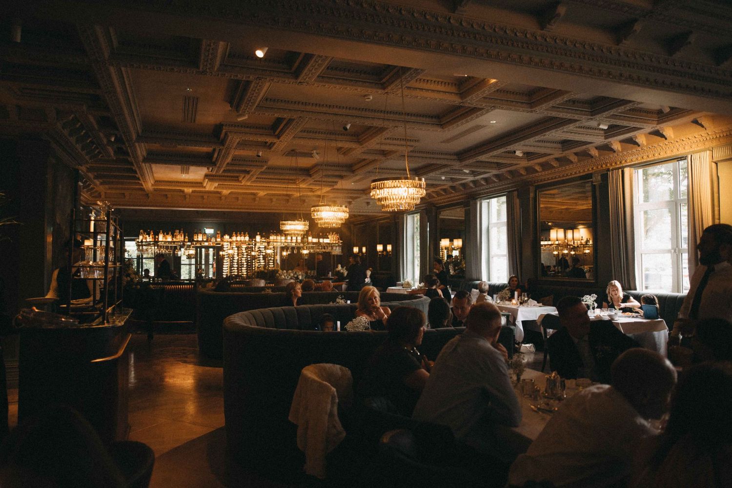 Elegant dimly lit wedding reception venue with ornate coffered ceiling, chandeliers, and guests dining at tables.