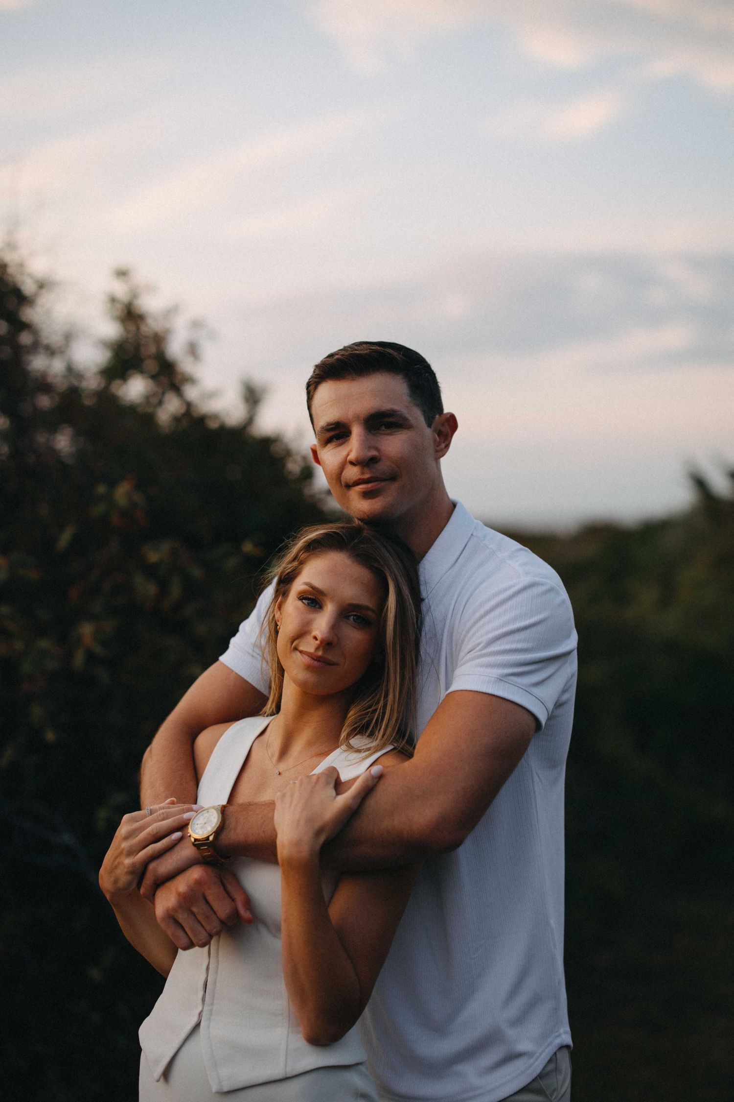 Man embracing woman from behind as they pose together at golden hour outdoors.