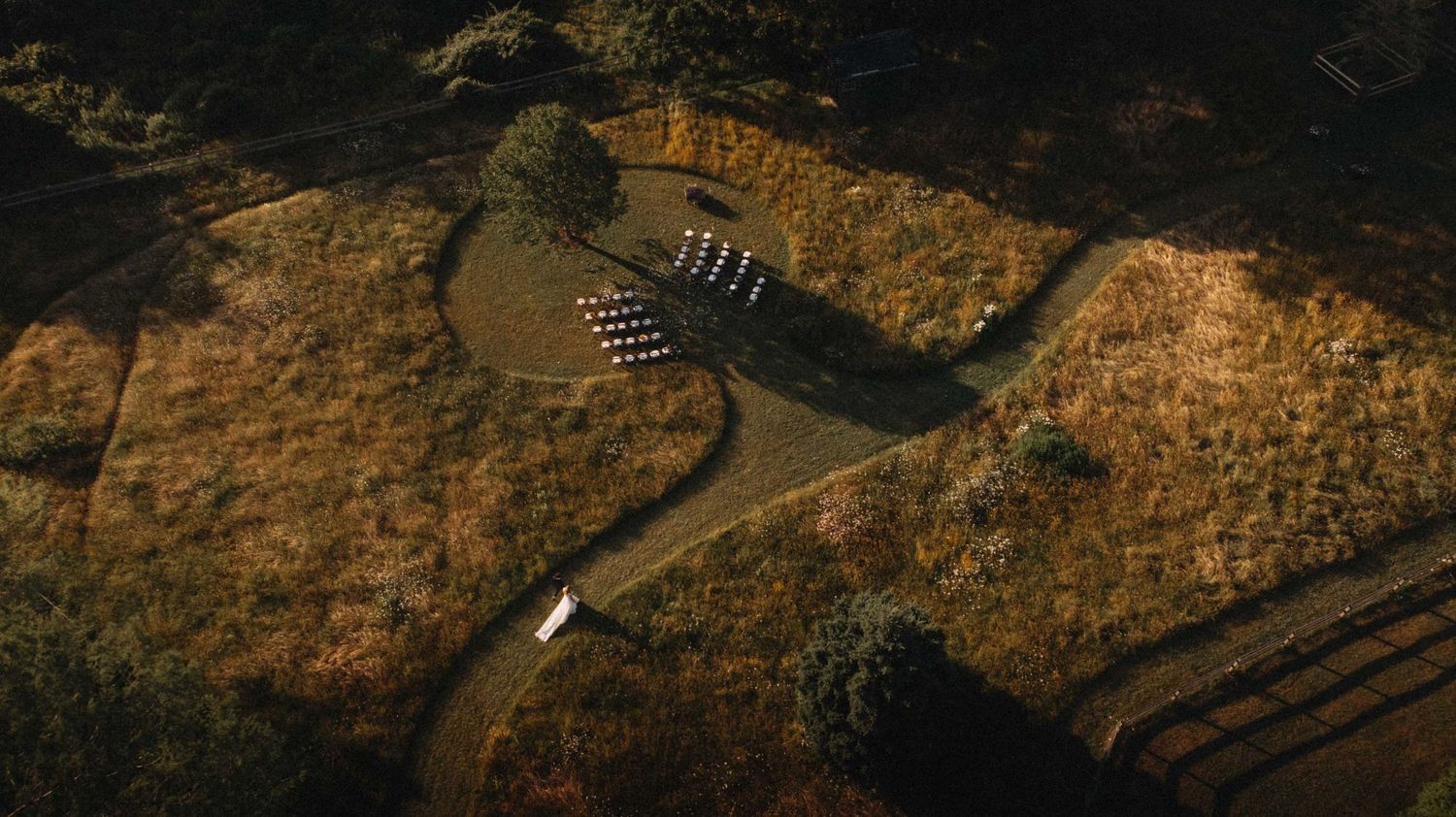 Aerial view of an outdoor wedding ceremony with white chairs arranged in rows on golden meadow.