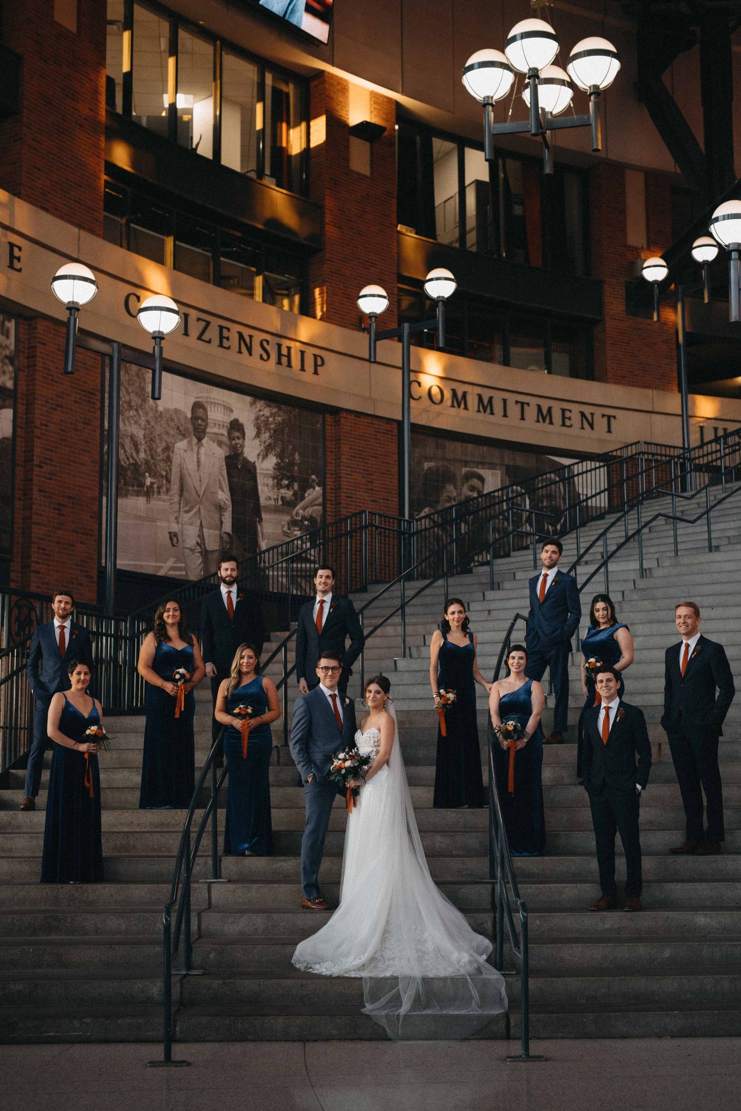 Wedding party poses on grand staircase outside building with Citizenship and Commitment inscriptions.