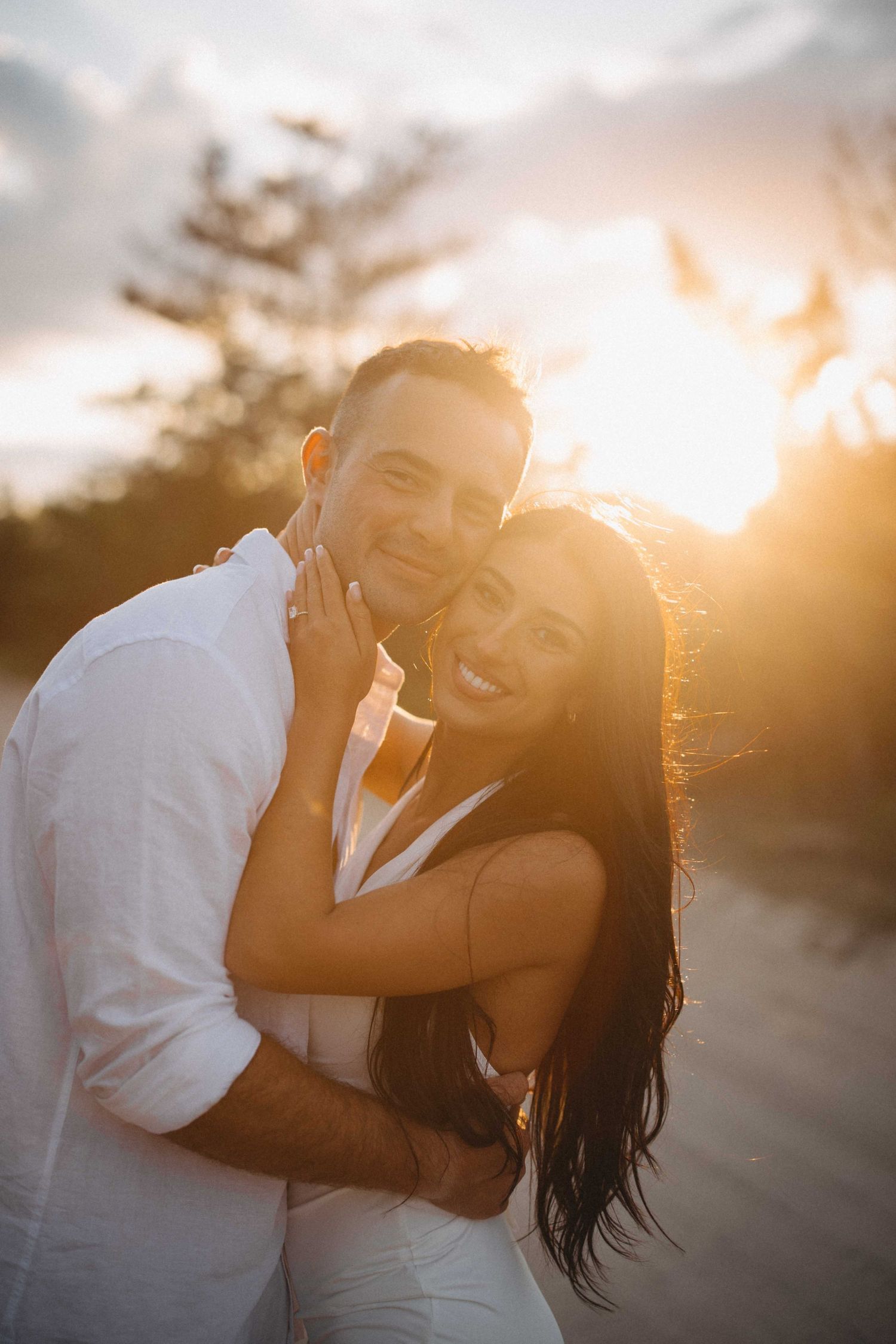 Happy couple embracing at golden hour sunset on a sandy beach path.