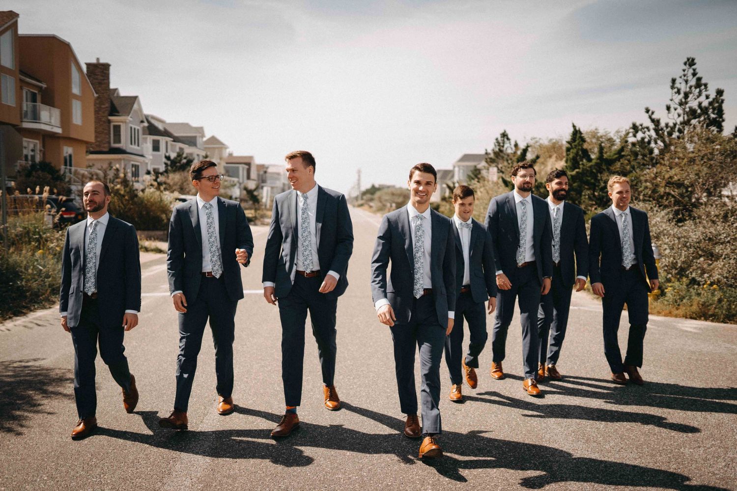 Groomsmen in navy suits walking confidently down a street on a sunny wedding day.