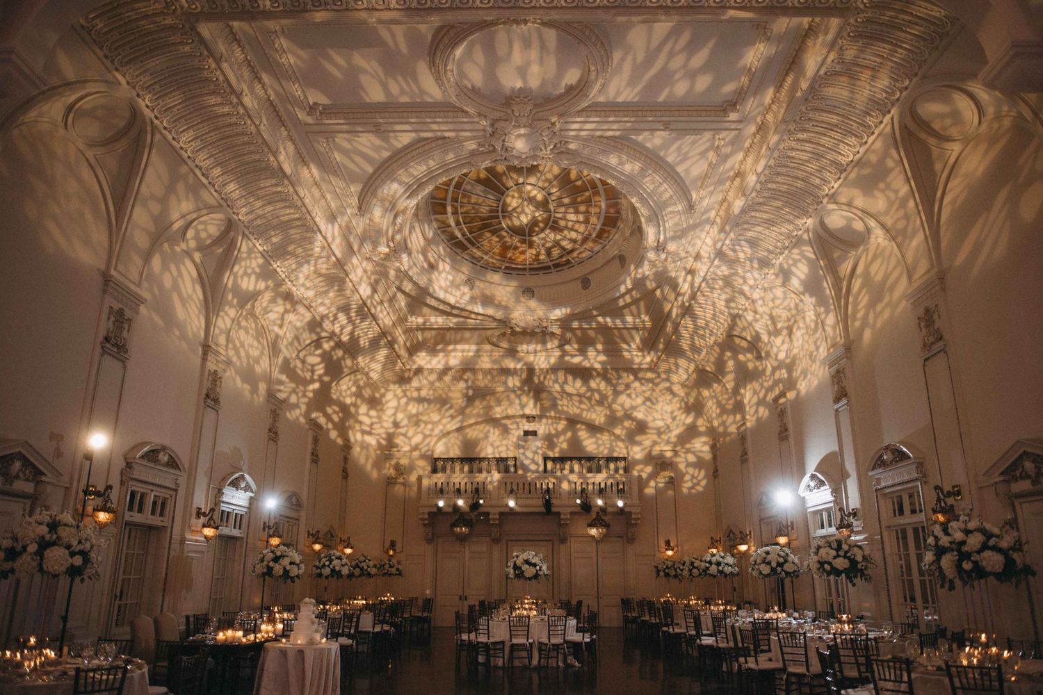 Luxurious wedding reception hall featuring intricate ceiling light patterns, chandelier, and elegantly set dining tables.