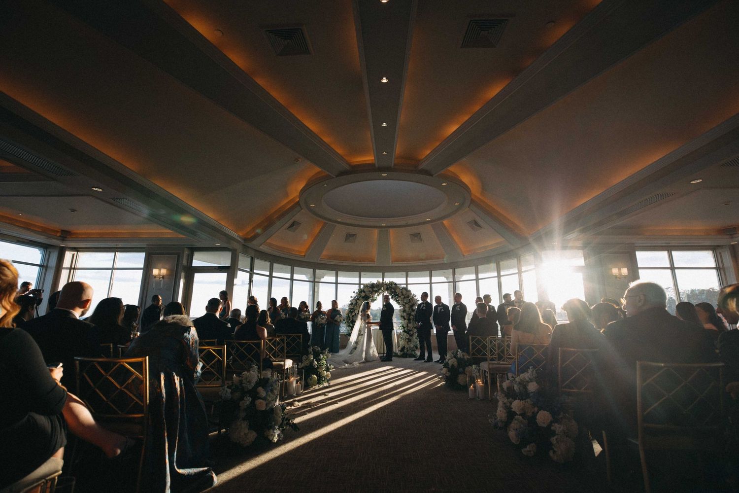 Wedding ceremony in panoramic venue with stunning sunlight streaming through floor-to-ceiling windows.