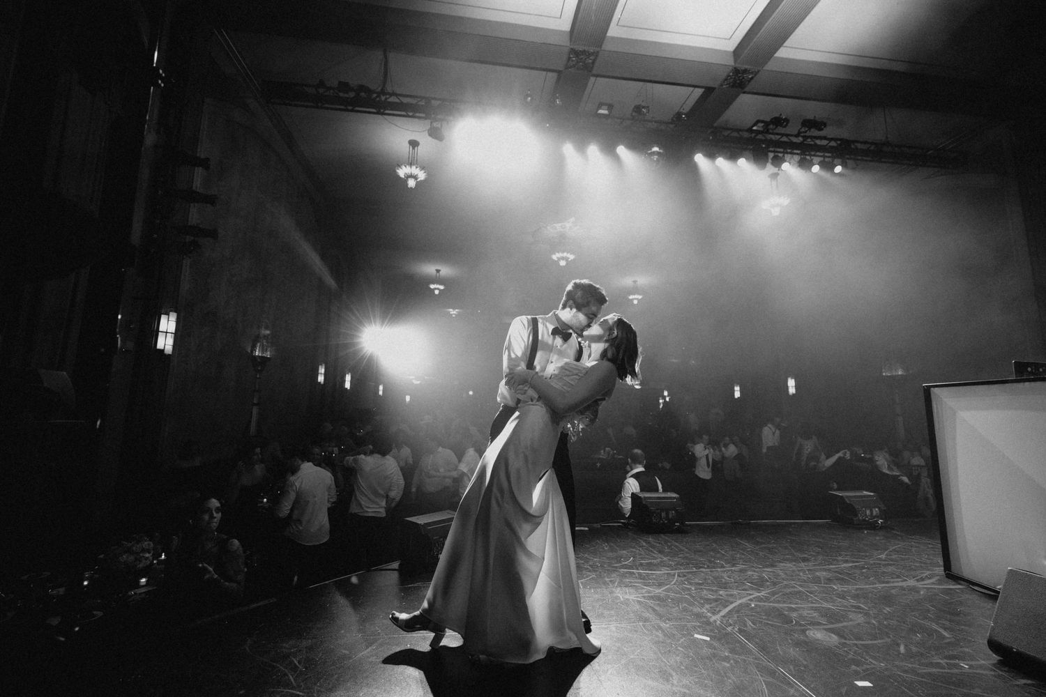 Black and white photo of bride and groom sharing first dance on a dramatic lit ballroom dance floor.