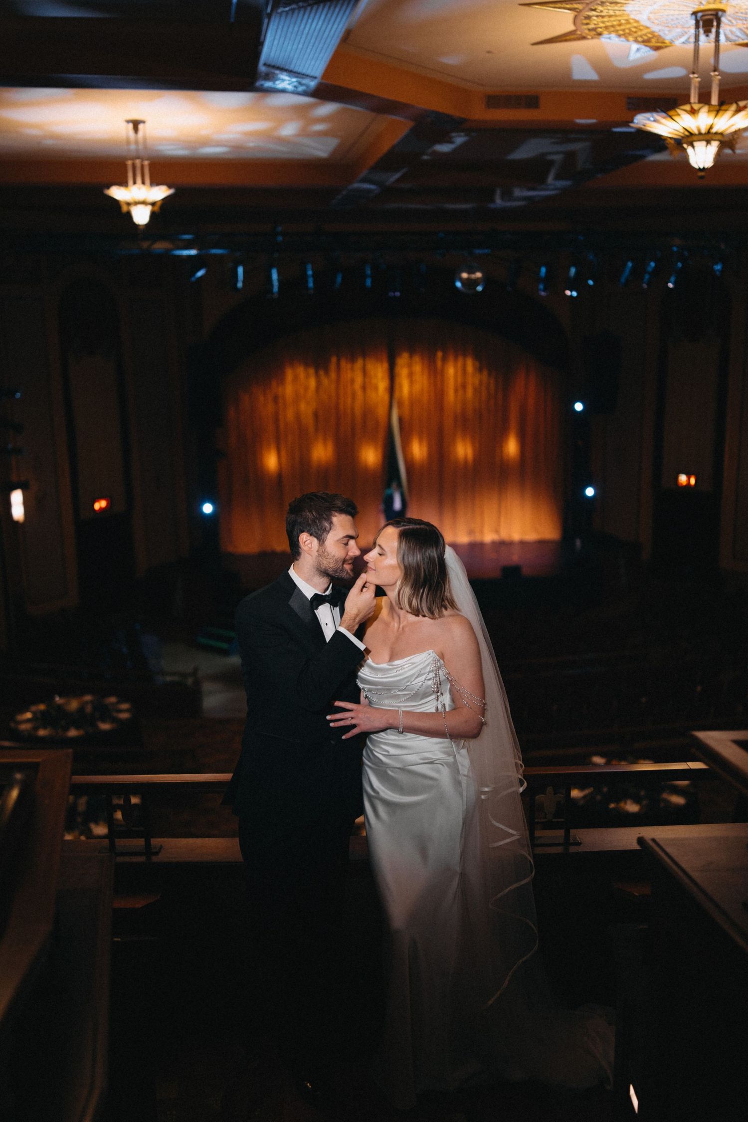 Bride and groom share a romantic moment in a dimly lit vintage theater venue on their wedding day.