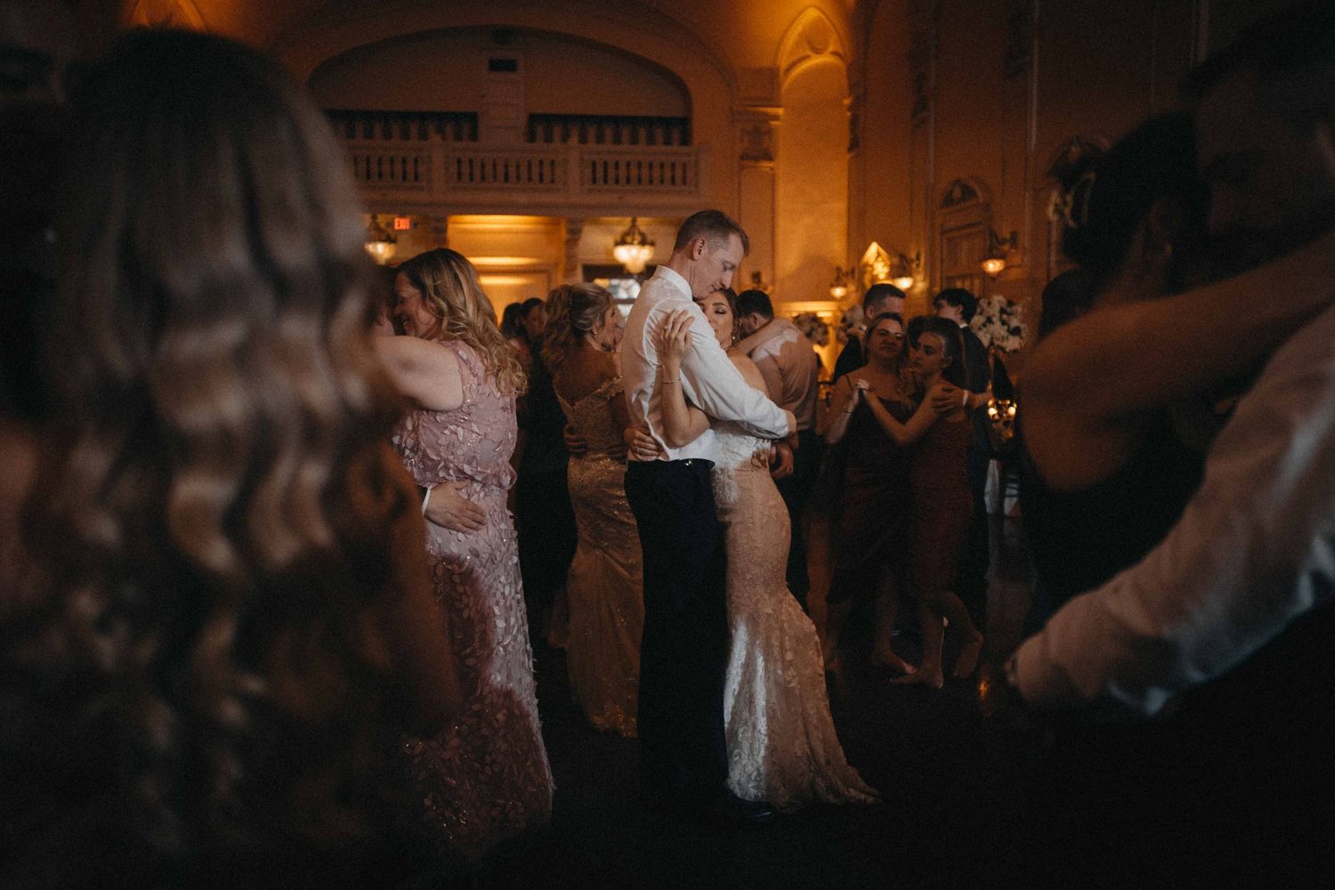 Bride and groom share intimate first dance surrounded by guests at warmly lit reception.