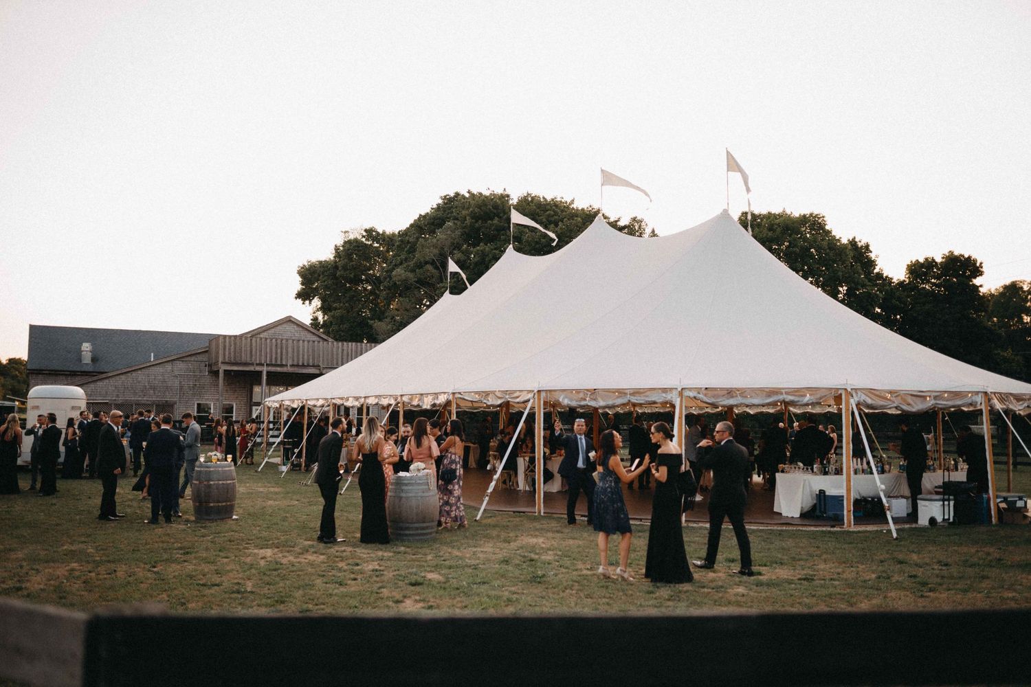 Guests mingle outside elegant white sailcloth tent at outdoor evening wedding reception on green lawn.