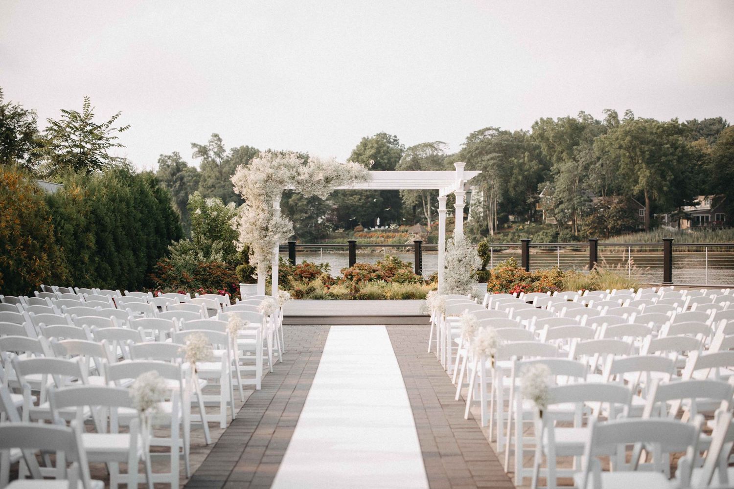 Outdoor wedding ceremony setup with white chairs, floral arch, and waterfront backdrop.
