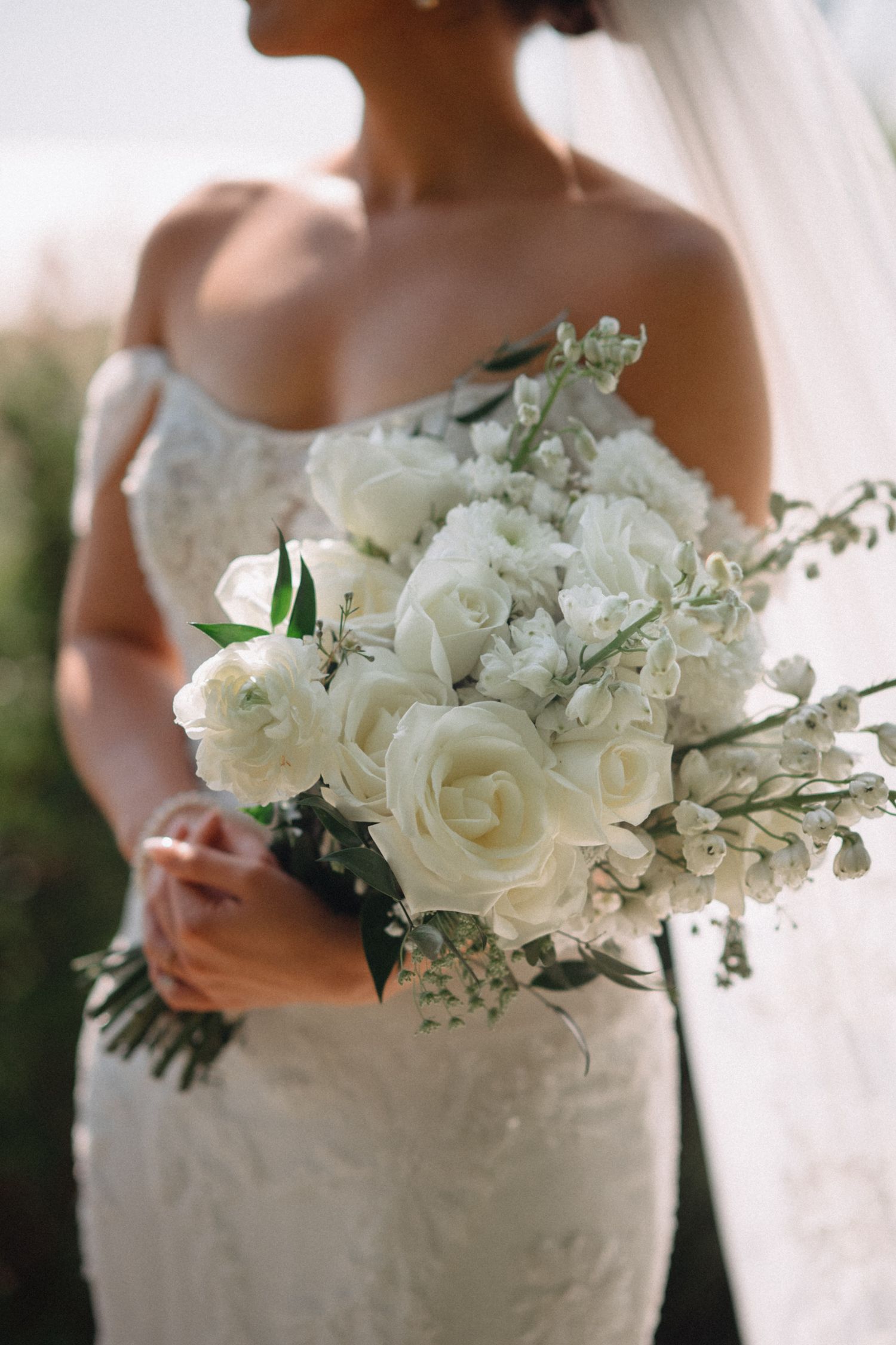 Bride holding a lush white rose and greenery wedding bouquet in a beaded lace bridal gown.
