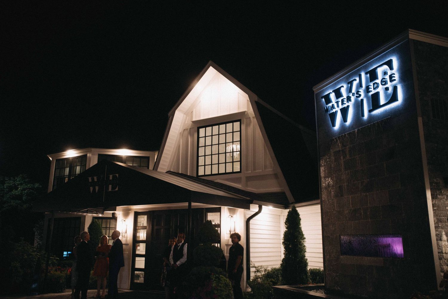 Elegant white barn wedding venue illuminated at night with glowing sign.