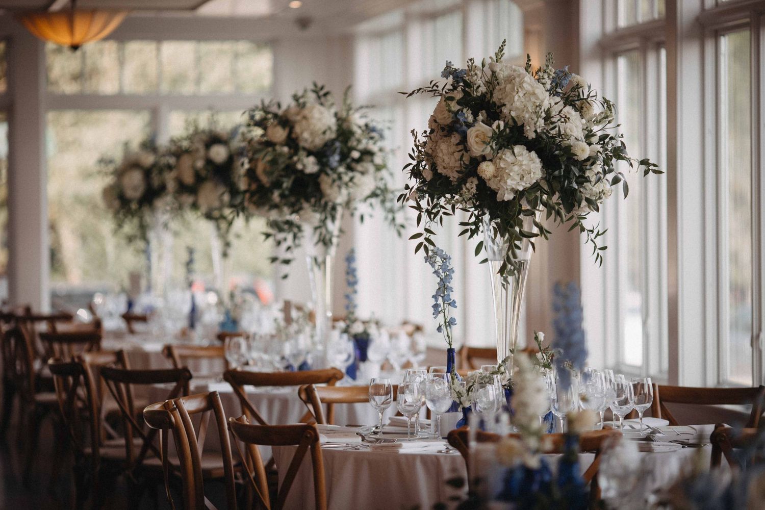 Elegant wedding reception tables adorned with tall white floral centerpieces and greenery.