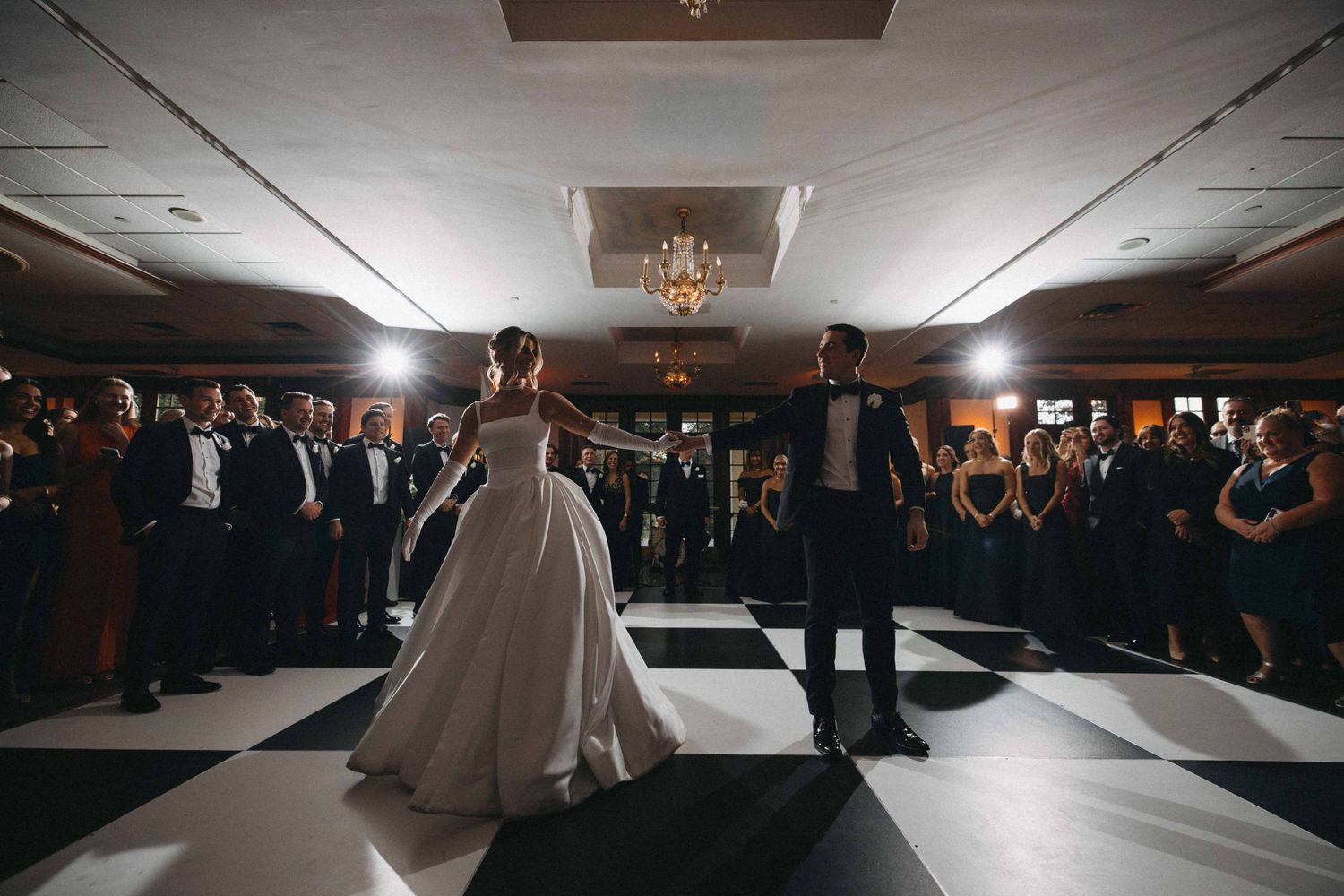 Bride and groom first dance on black and white checkered ballroom floor.