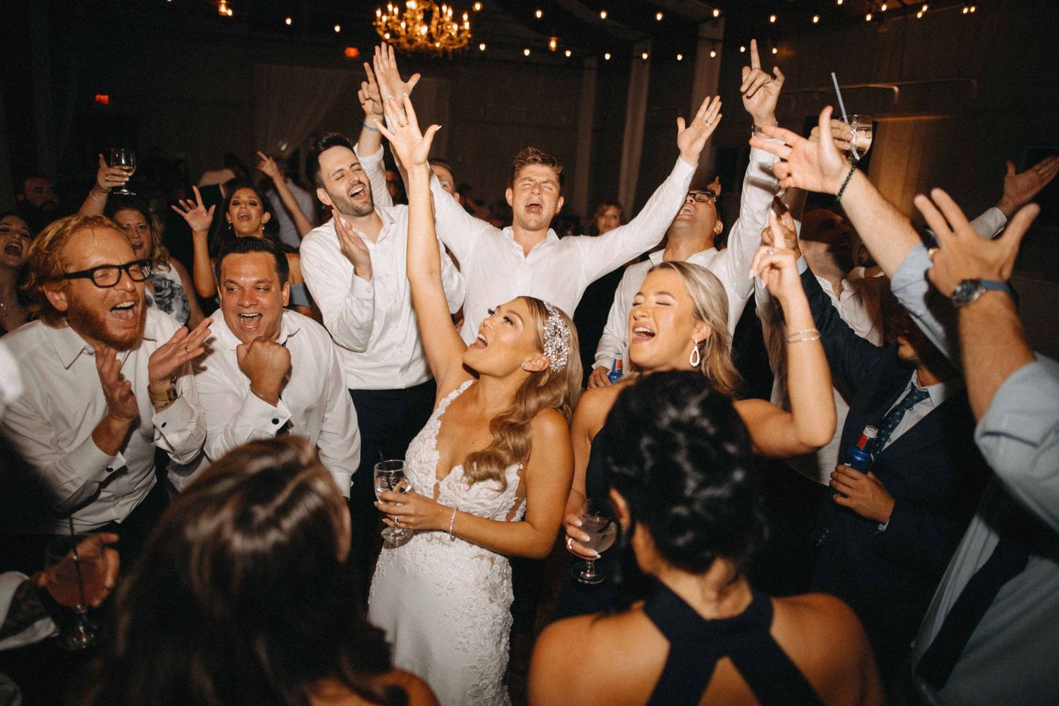 Joyful bride surrounded by cheering wedding guests on a lively reception dance floor.