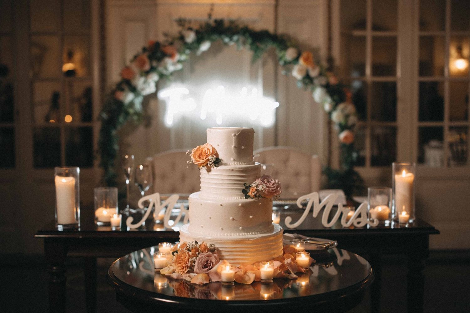 Elegant four-tier wedding cake displayed on a table with Mr. and Mrs. signs and candles.