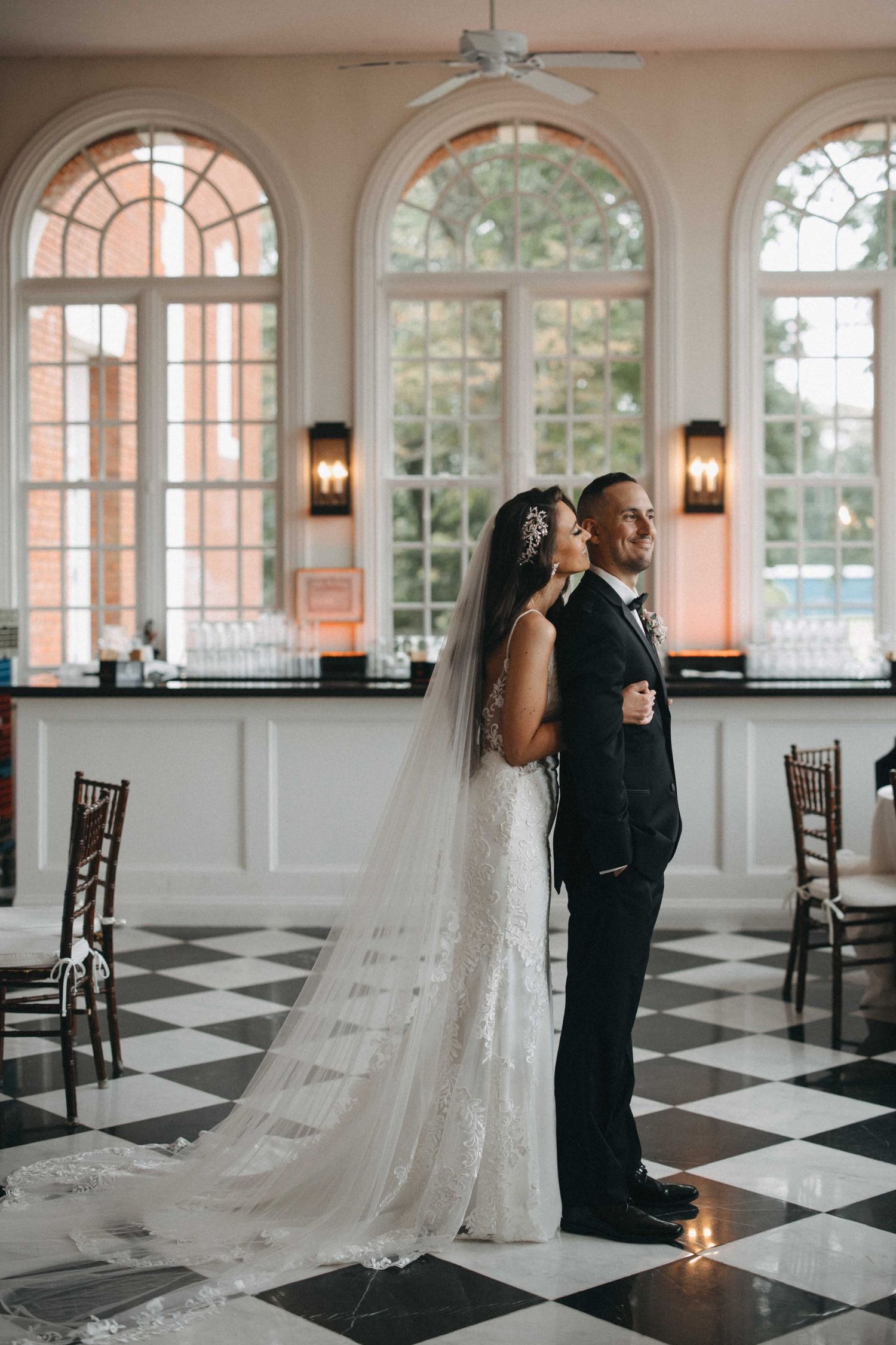 Bride and groom embrace on a black and white checkered floor in a grand ballroom.