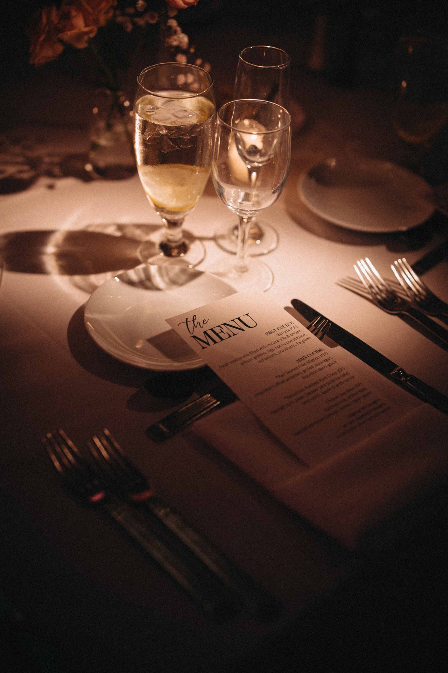 Elegant wedding reception table setting with menu card, champagne glasses, and candlelight.