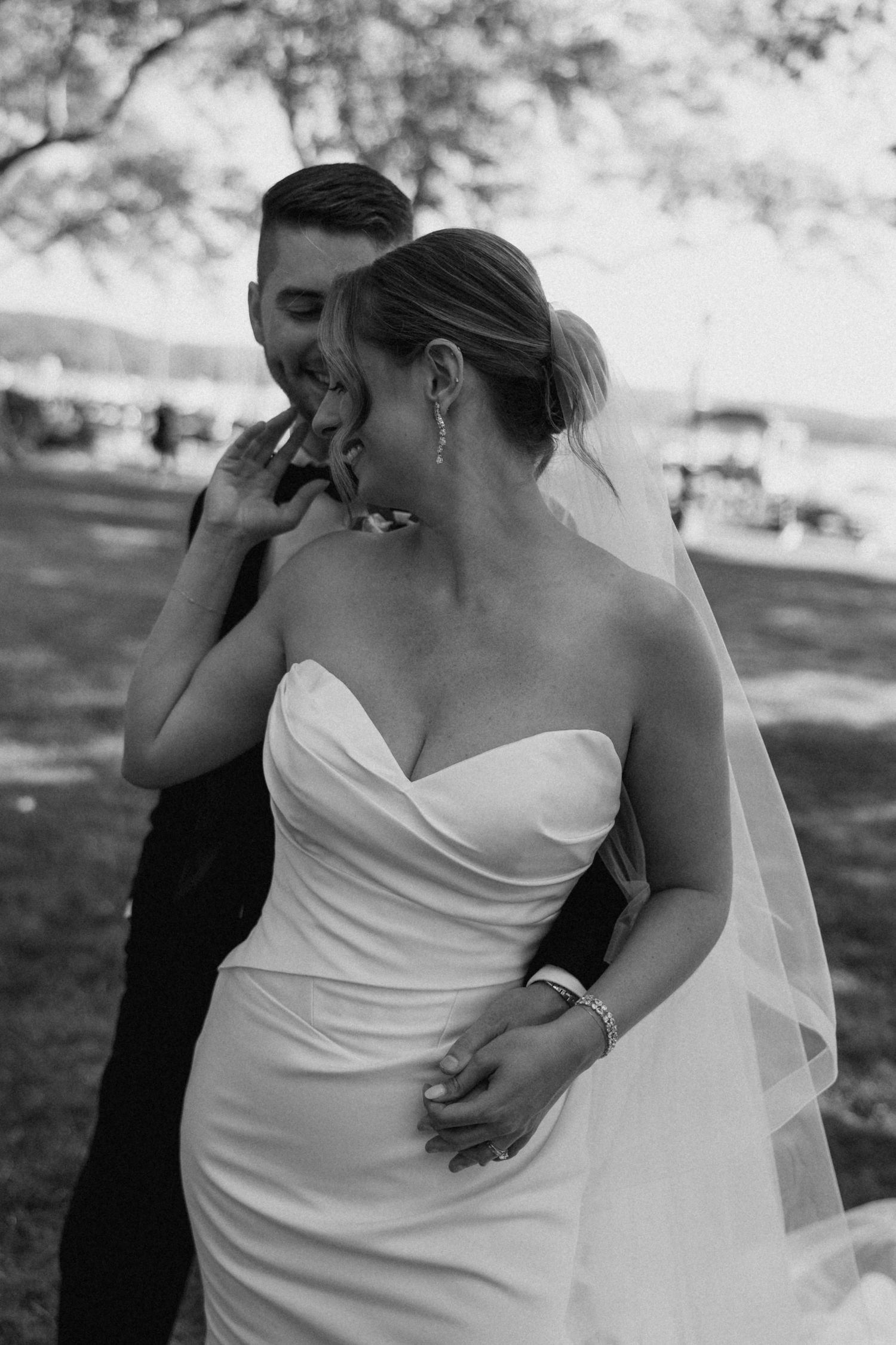 Black and white photo of a bride and groom sharing an intimate moment outdoors, bride in strapless gown with veil.