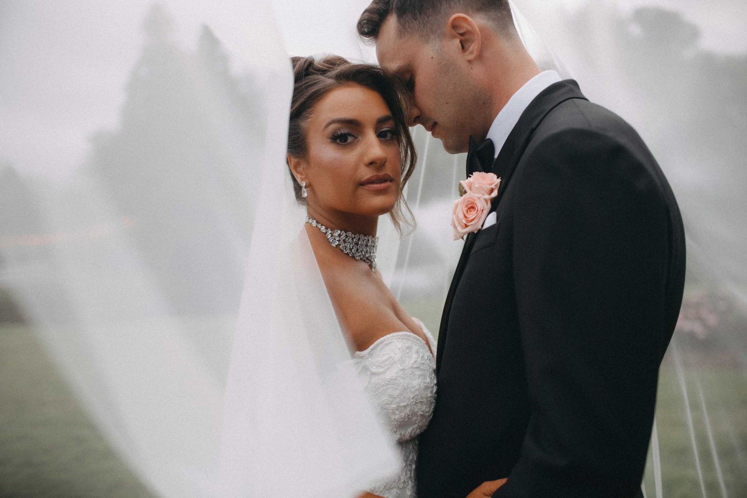 Bride and groom sharing an intimate moment under a flowing veil on their wedding day.