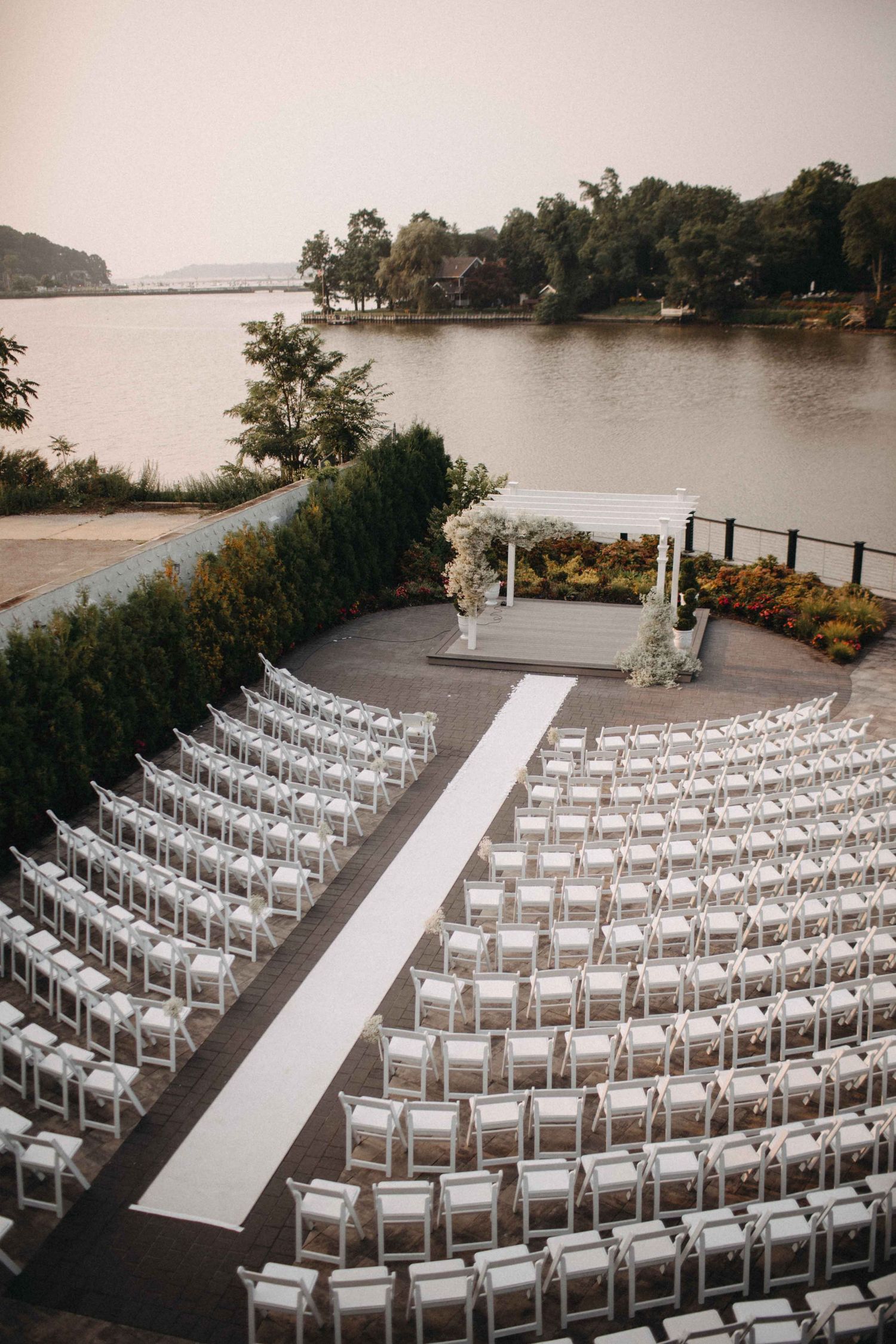 Rows of white chairs arranged in a semicircle at an elegant outdoor waterfront wedding venue.