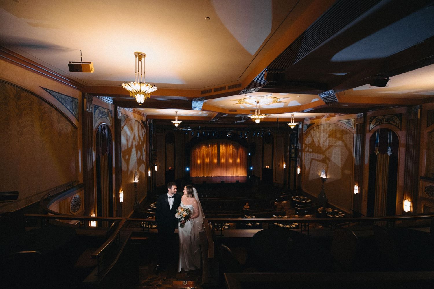 Bride and groom share a romantic moment in an elegant, dimly lit wedding venue with warm chandelier lighting.