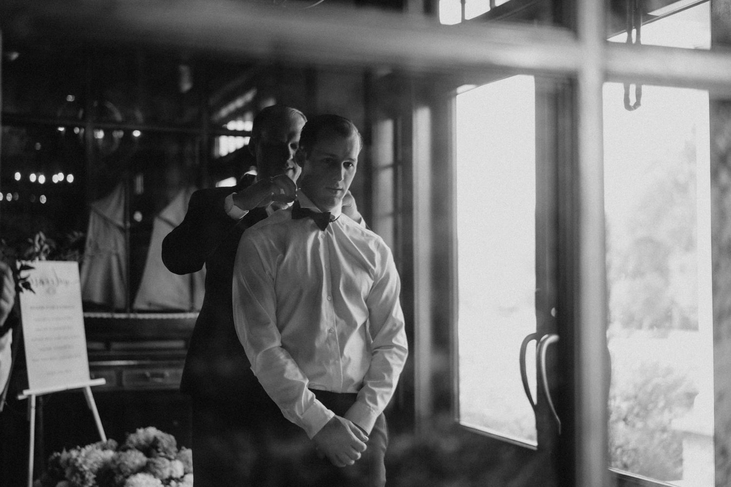 Groom adjusting bow tie in mirror before wedding ceremony in black and white photo.